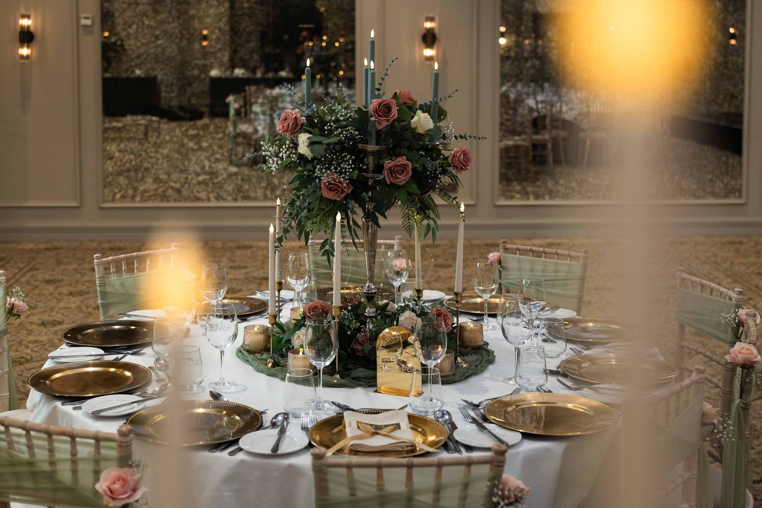 Elegant wedding reception table with floral centerpiece, candles, gold chargers, and glassware in a grand venue. Dunboyne Castle