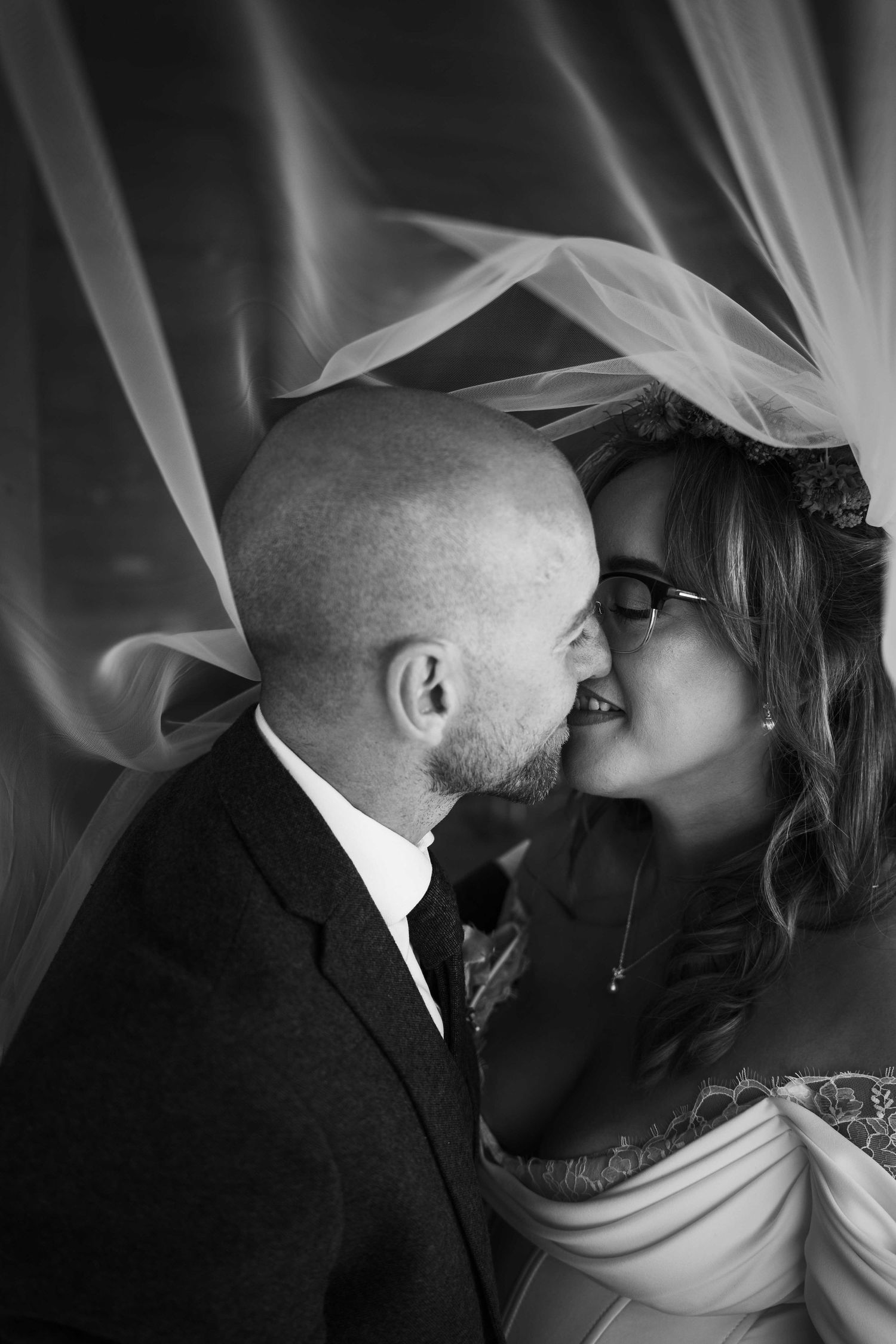 Black and white close-up of bald groom and bride about to kiss beneath a flowing veil. Irish wedding photography. Mountain View, Kilkenny