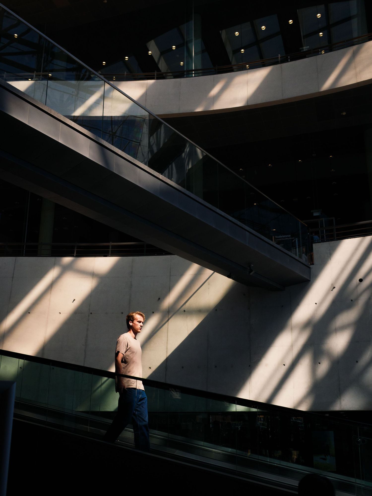 Man standing on escalator inside modern building with dramatic light and shadow patterns on walls.