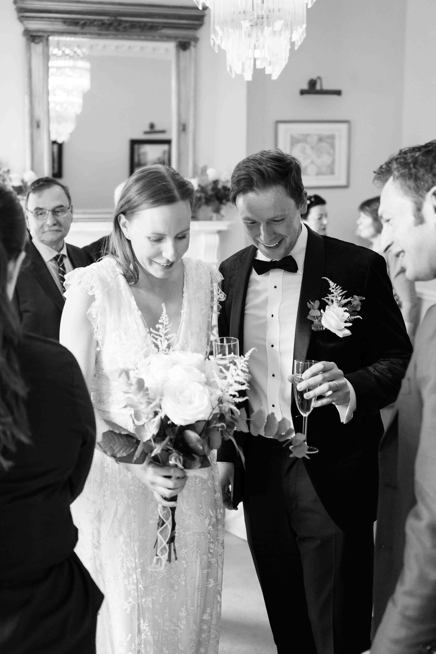 Black and white photo of a smiling bride and groom holding champagne glasses at their wedding reception. Dunboyne Castle