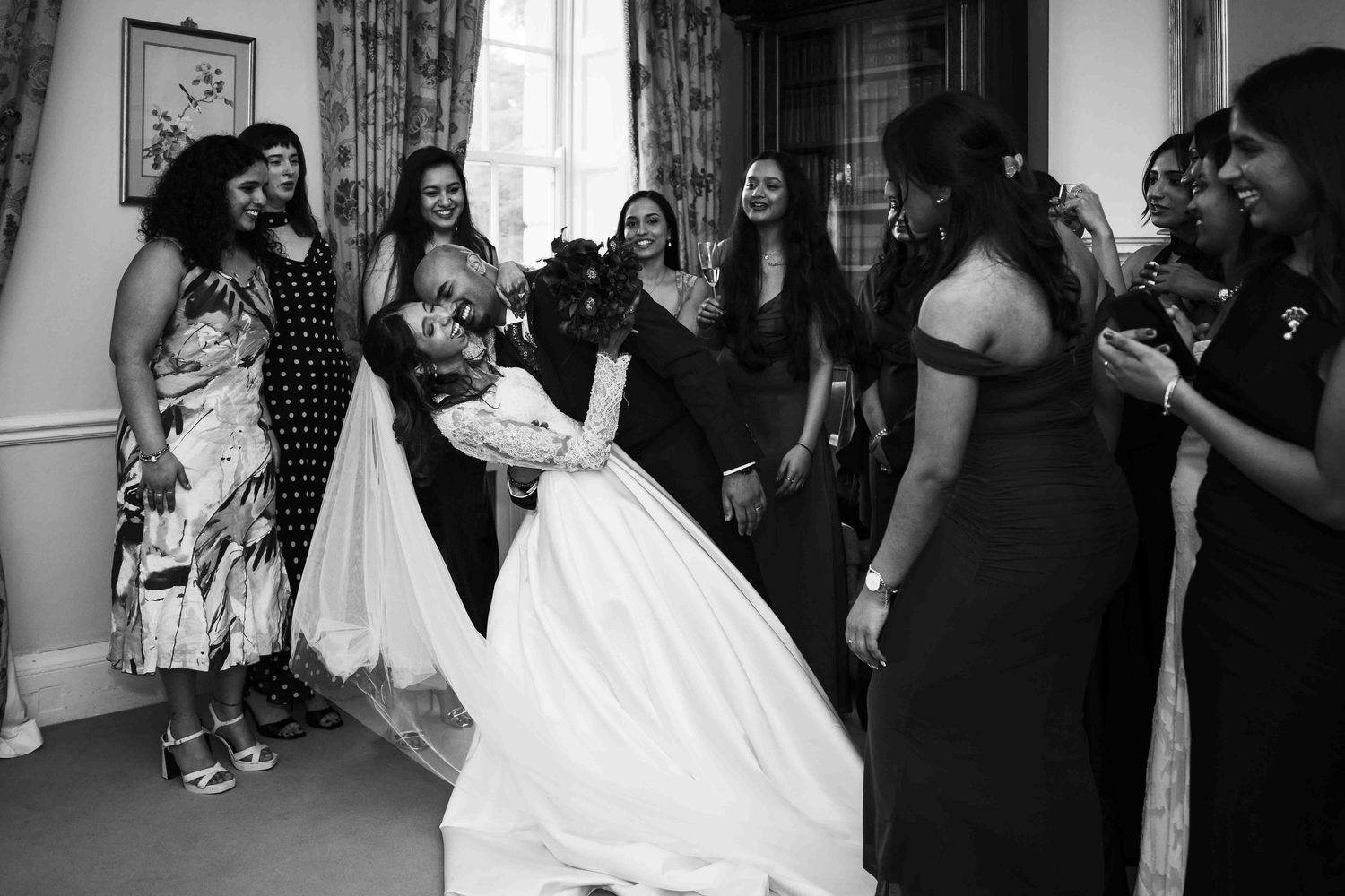 Black and white photo of a bride in a white gown surrounded by smiling bridesmaids in a elegant room. Dunboyne Castle