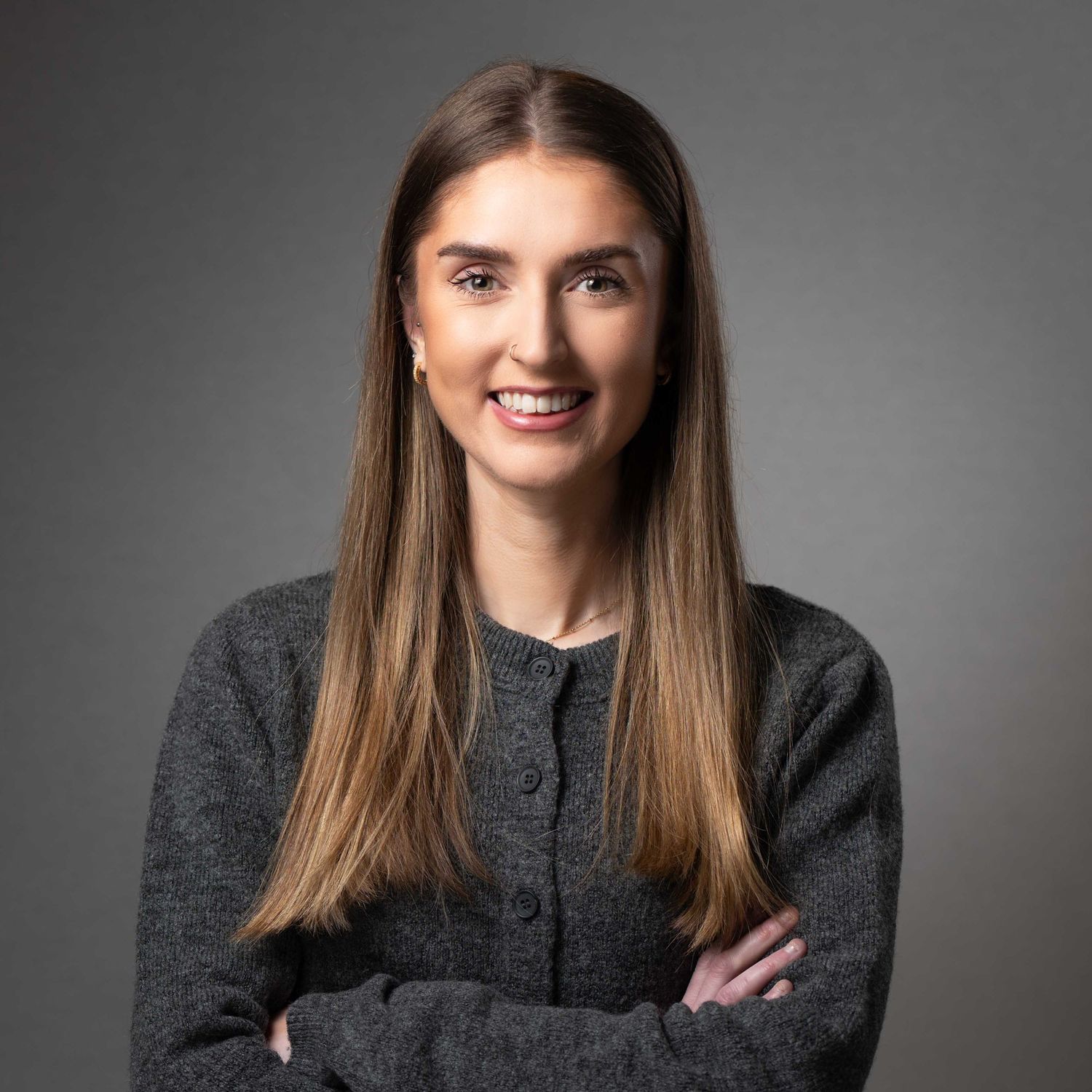 Smiling professional woman with long hair in gray cardigan posing for corporate headshot photography. Headshot Photography Ireland