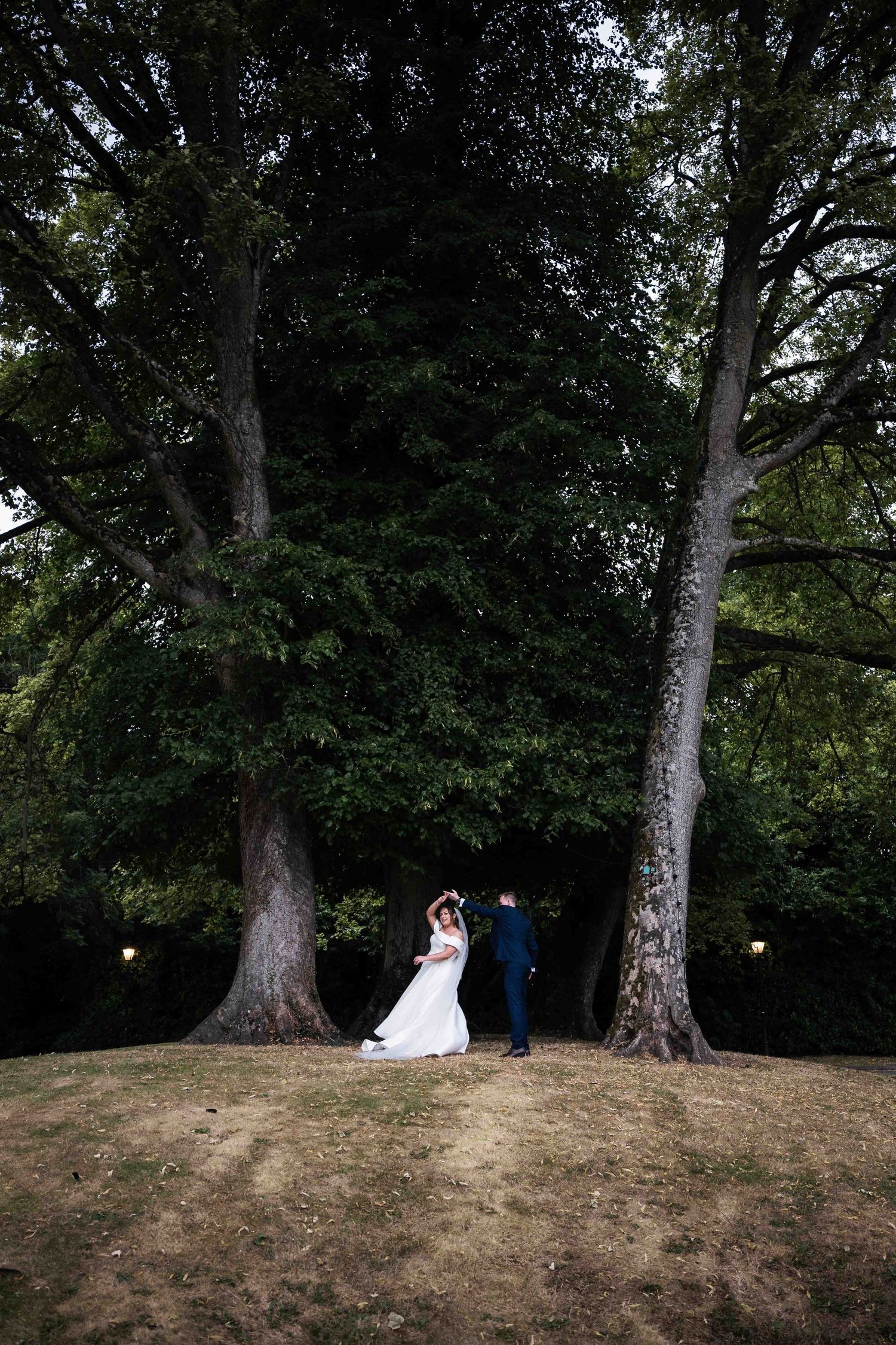 Bride and groom standing between two tall trees in a lush garden during their outdoor wedding. Irish wedding photography. Dunboyne Castle
