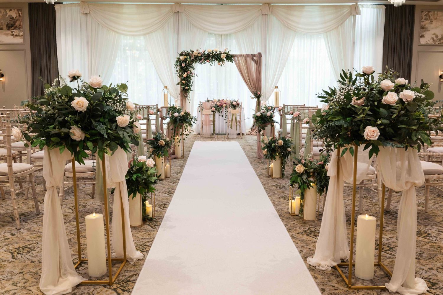 Elegant wedding ceremony aisle with white runner, floral arrangements, candles, and a floral arch backdrop. Dunboyne Castle