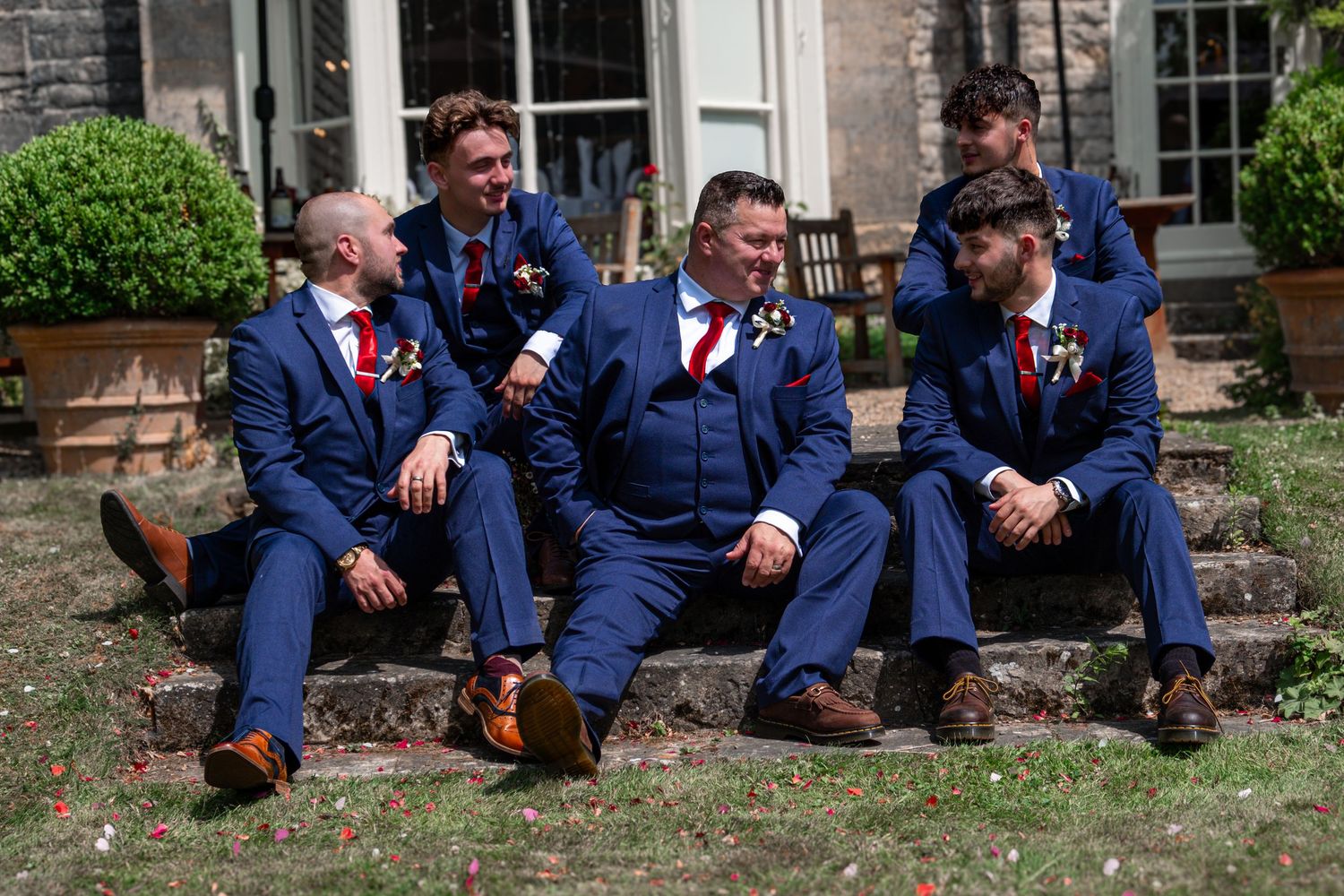 Groomsmen sitting with groom on steps at the wedding venue.