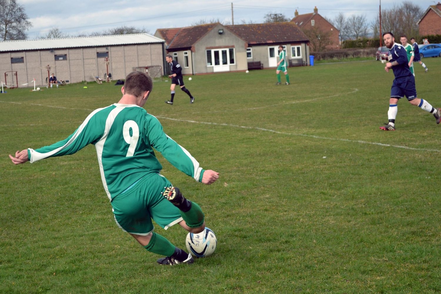 Football player in a green number 12 shirt kicking the ball during a North Yorkshire league match.