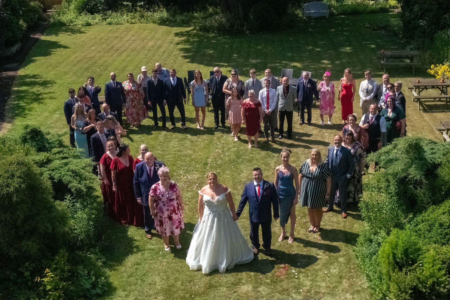 Wedding guests stood in the shape of a love heart in the garden of the wedding venue.