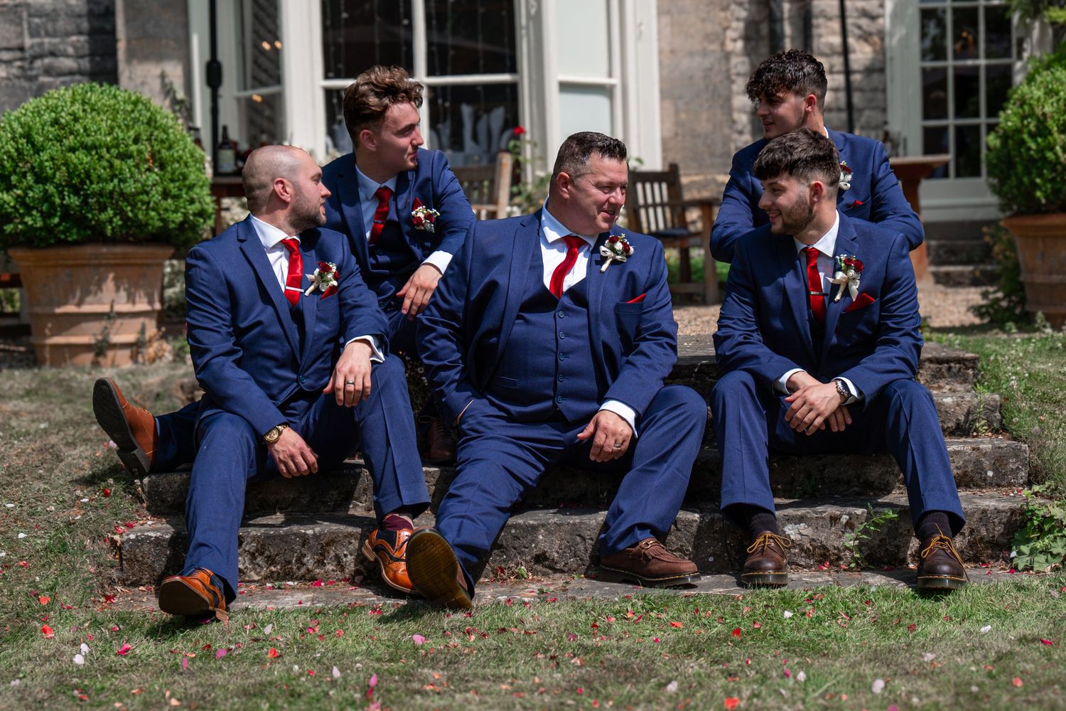 Groom and his groomsmen sat on the steps of the garden of the wedding venue.