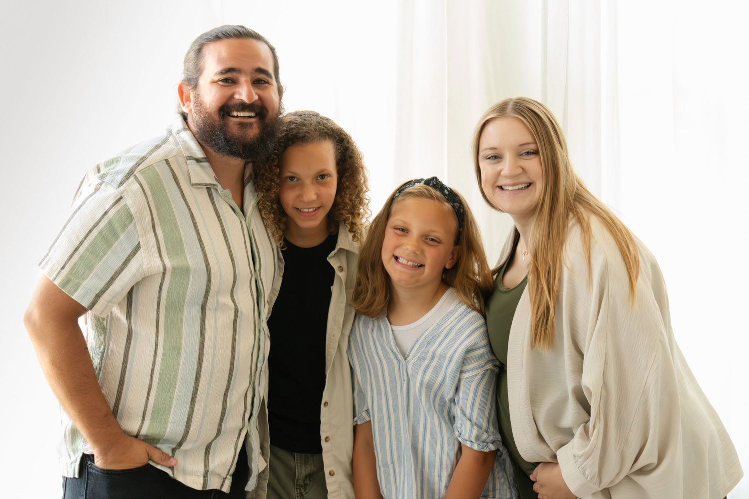 A smiling family of four poses together in a bright white studio setting for a professional portrait photo.
