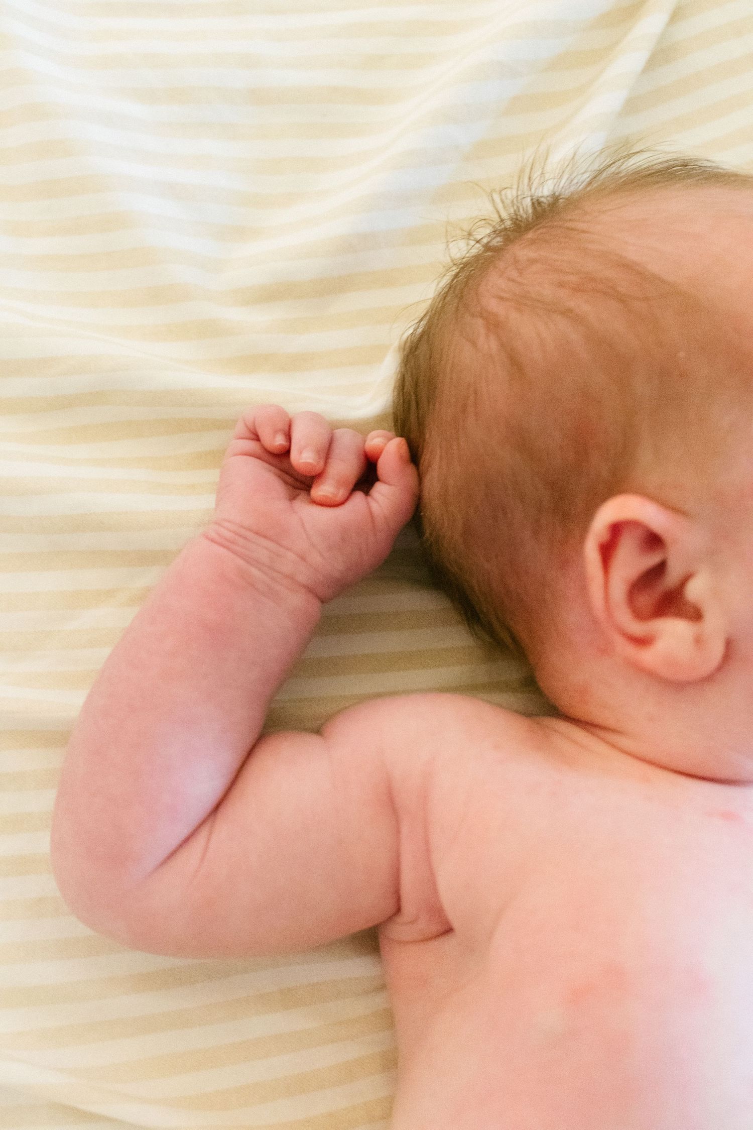 Close-up of sleeping newborn baby lying on striped blanket with tiny fist raised.