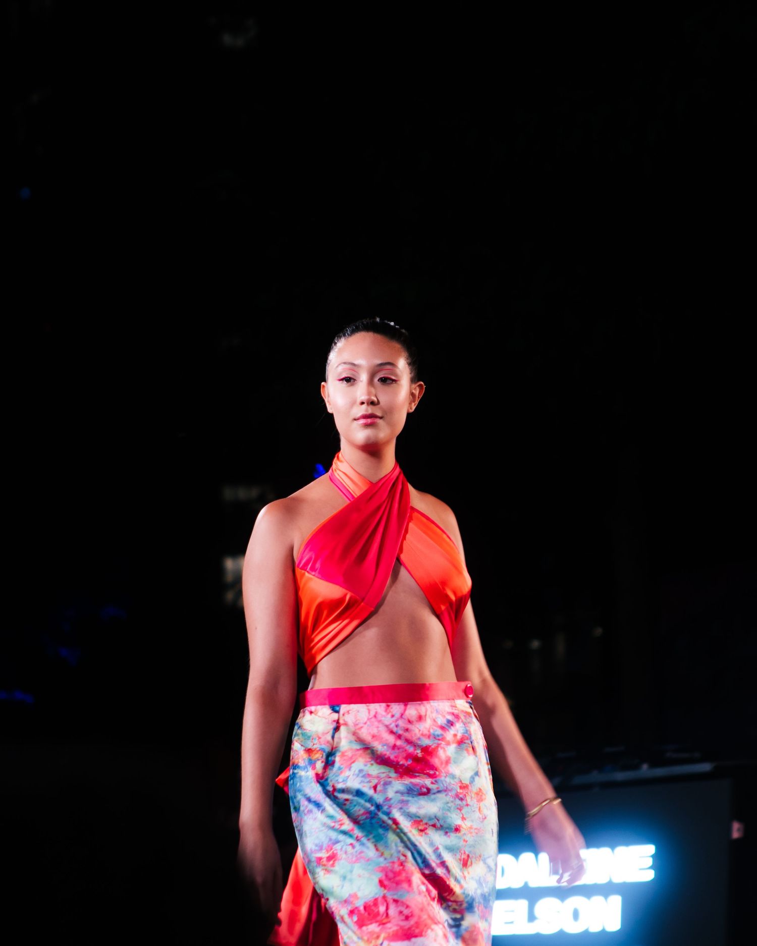 Model in a vibrant pink patterned outfit under stage lighting, runway fashion photography by HAMIDI Photography.