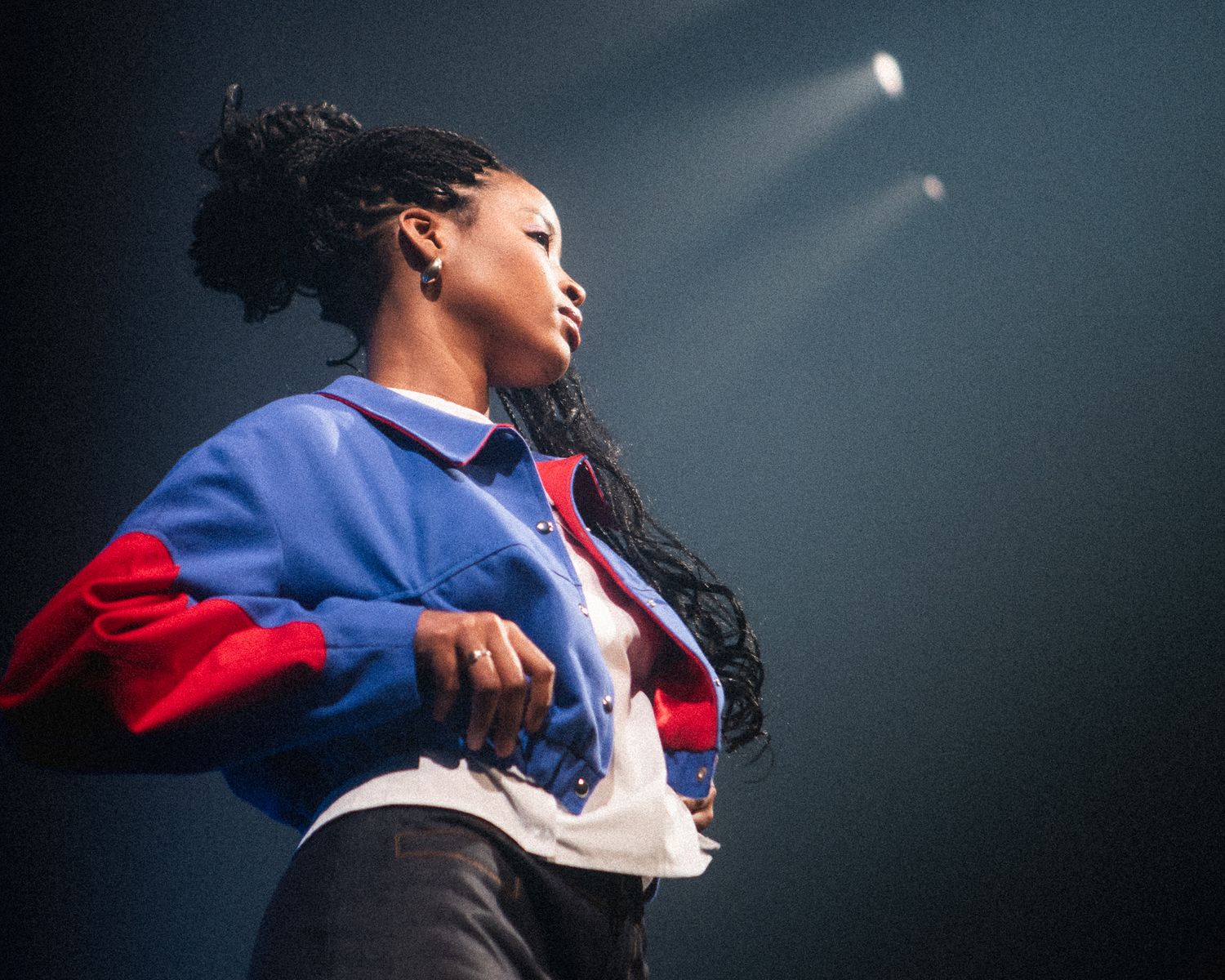 Model on stage under dramatic stage lighting wearing a bold red and blue jacket, fashion photography by HAMIDI Photography.