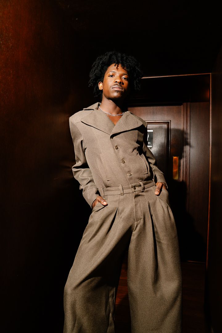 Model in a tan coat walking the runway under warm stage lighting, fashion photography by HAMIDI Photography.