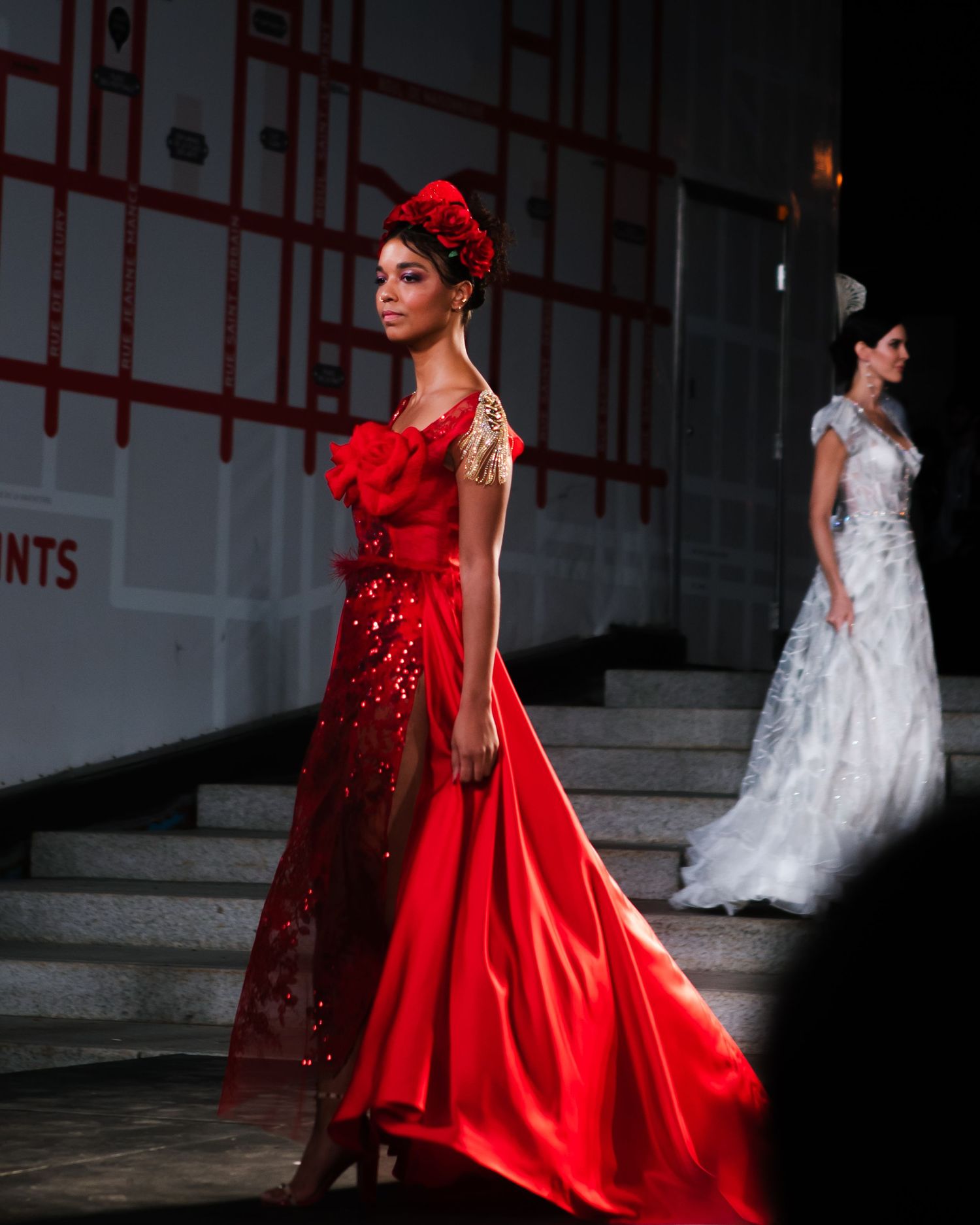 Model in a bold red gown walking the runway with a flowing white garment, fashion editorial photography by HAMIDI Photography.