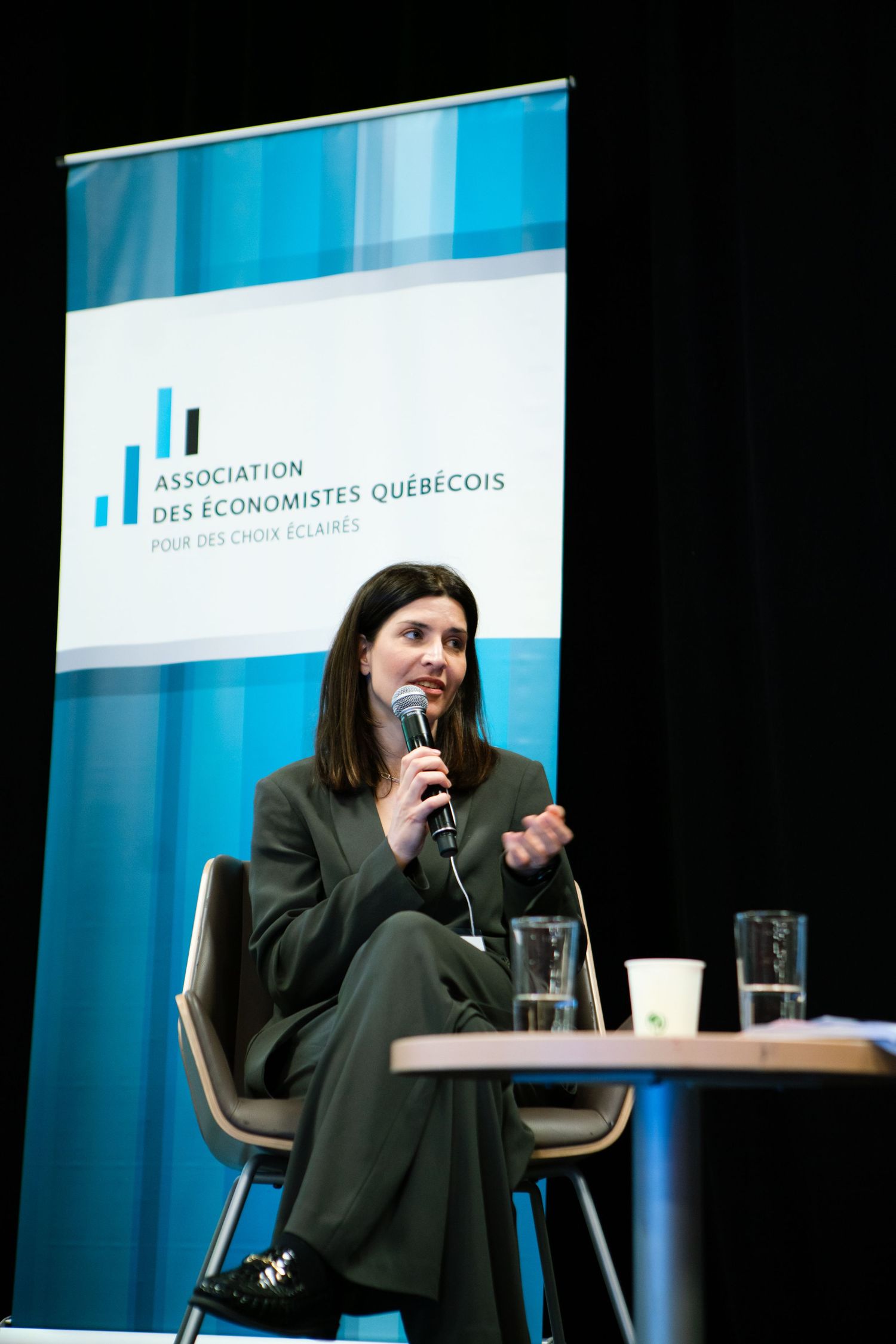 Speaker standing at a podium in front of a branded blue backdrop, conference photography by HAMIDI Photography.
