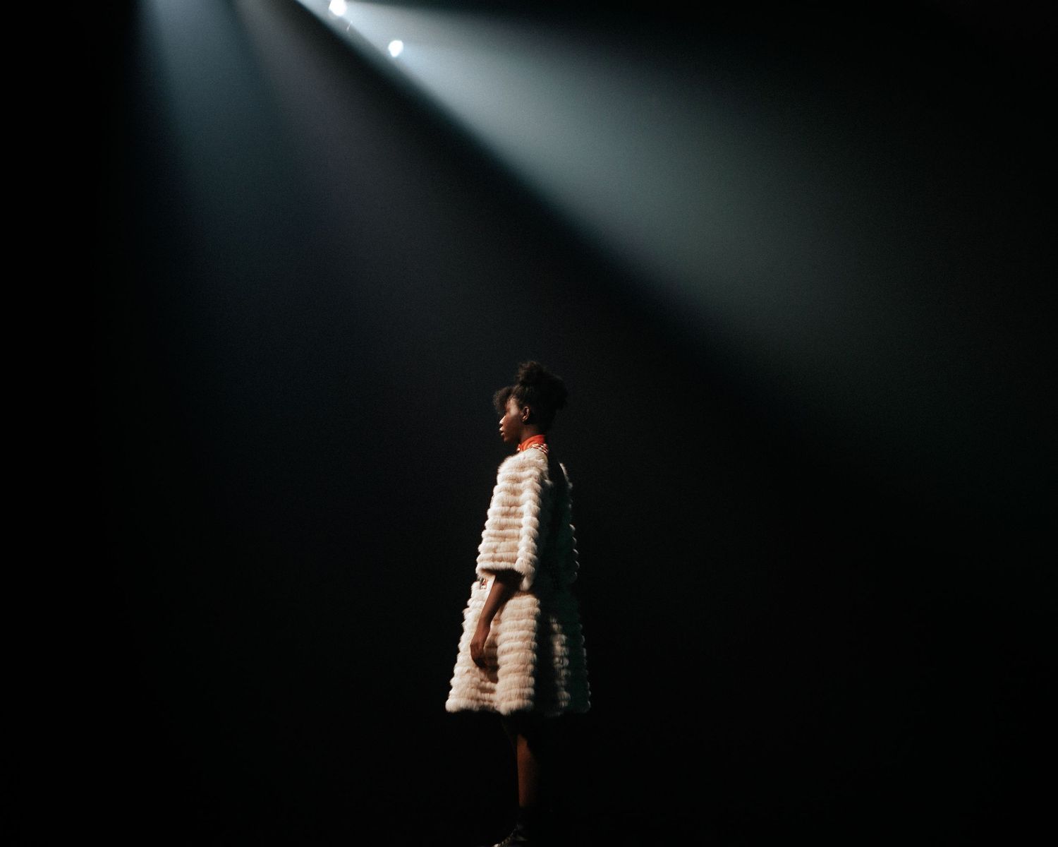 Model silhouetted under a single spotlight on stage, dramatic runway fashion photography by HAMIDI Photography.
