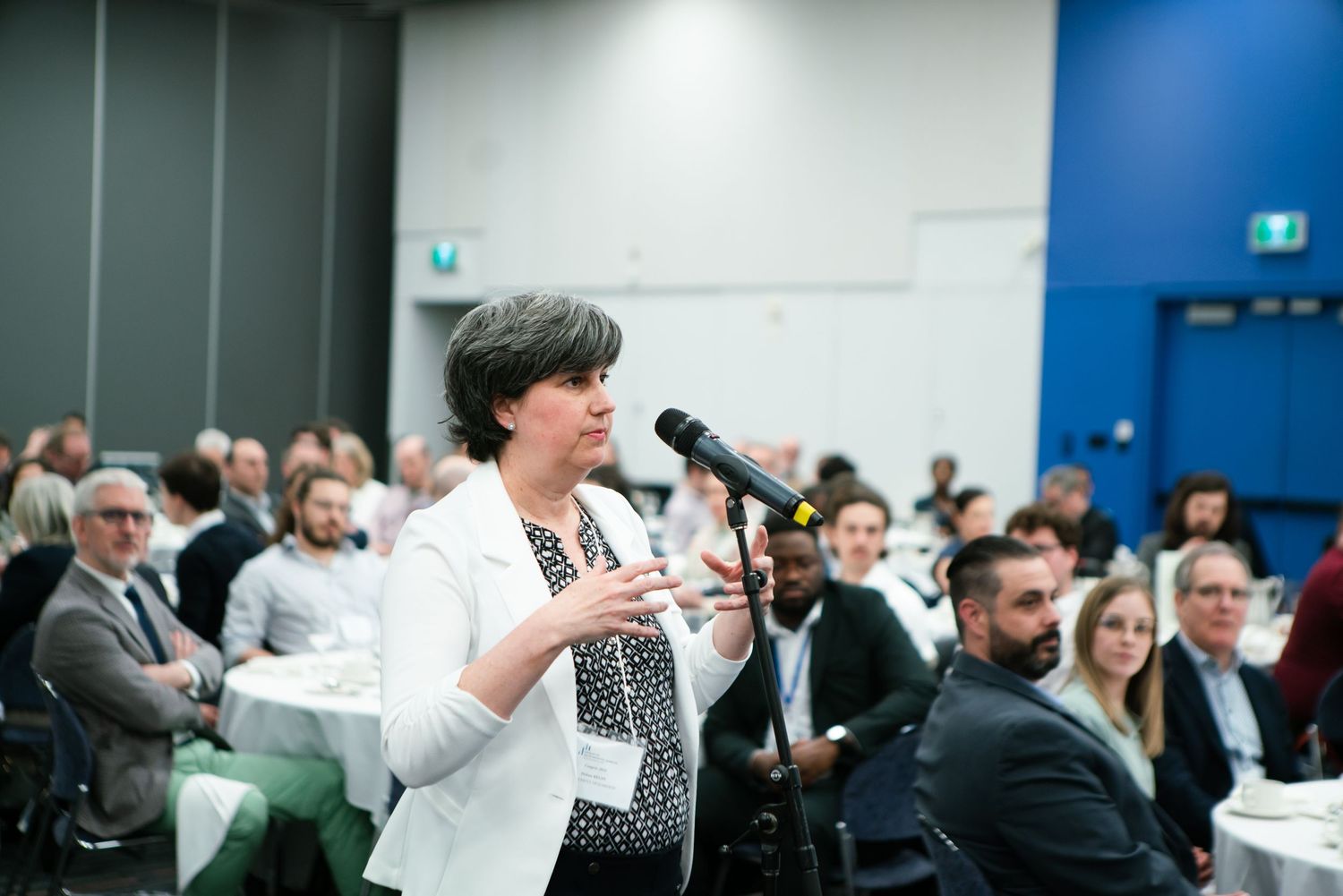 Woman speaking into a microphone from the audience during a conference Q&A, event photography by HAMIDI Photography.