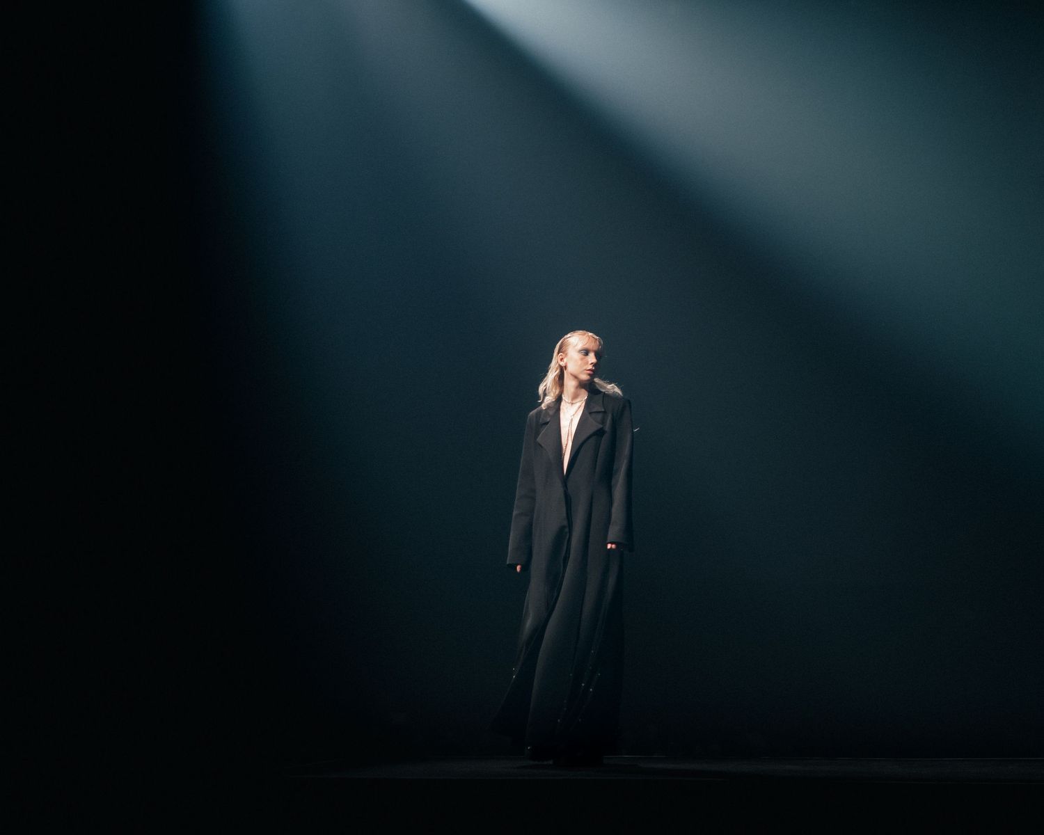 Model standing under a blue spotlight on a dark stage, dramatic fashion photography by HAMIDI Photography.