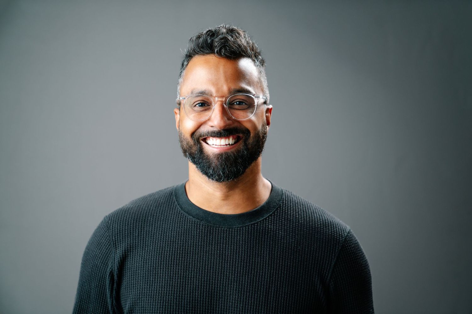 Studio headshot of Gavin Seal smiling against a gray backdrop, photography by HAMIDI Photography.