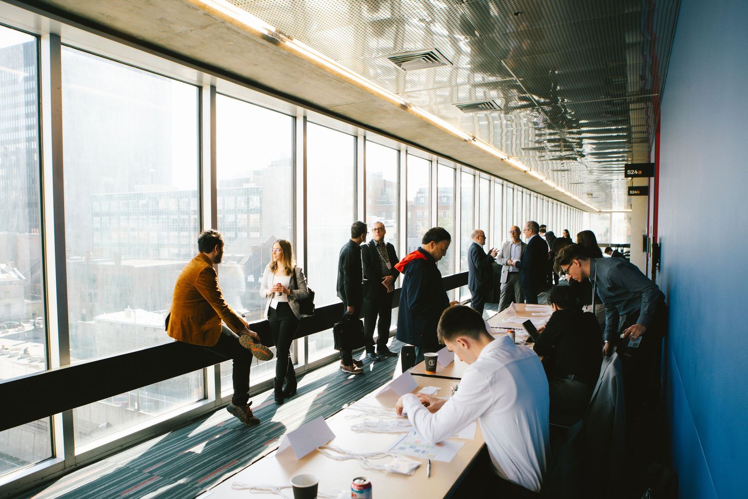 Colleagues standing in discussion by floor-to-ceiling windows, corporate photography by HAMIDI Photography.