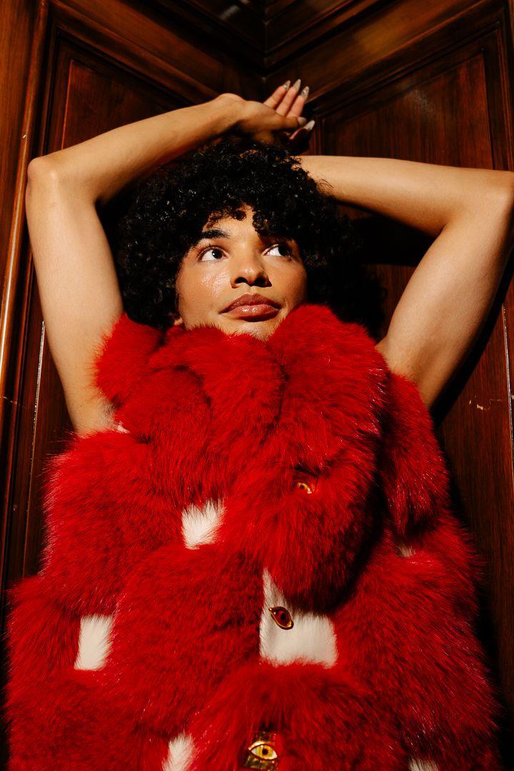 Model in a red outfit striking a dramatic pose under warm stage lighting, fashion photography by HAMIDI Photography.
