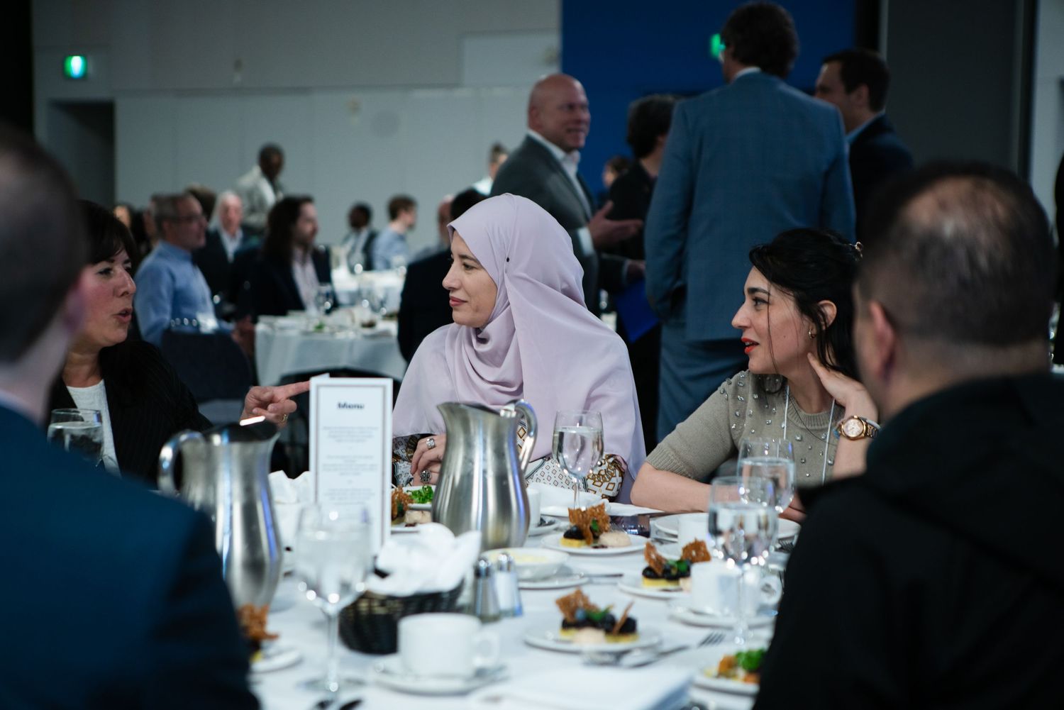 Guests seated and conversing at a formal corporate dinner event, photography by HAMIDI Photography.