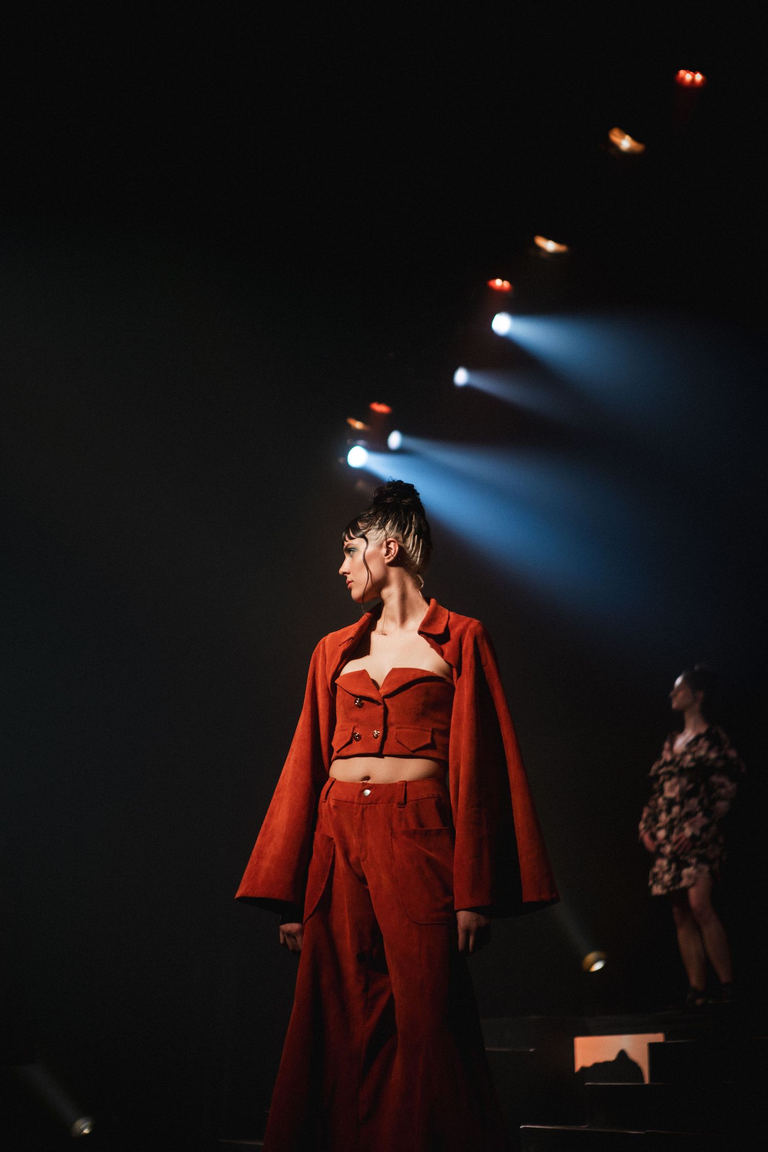 Model in a warm red outfit lit by golden stage light, fashion runway photography by HAMIDI Photography.