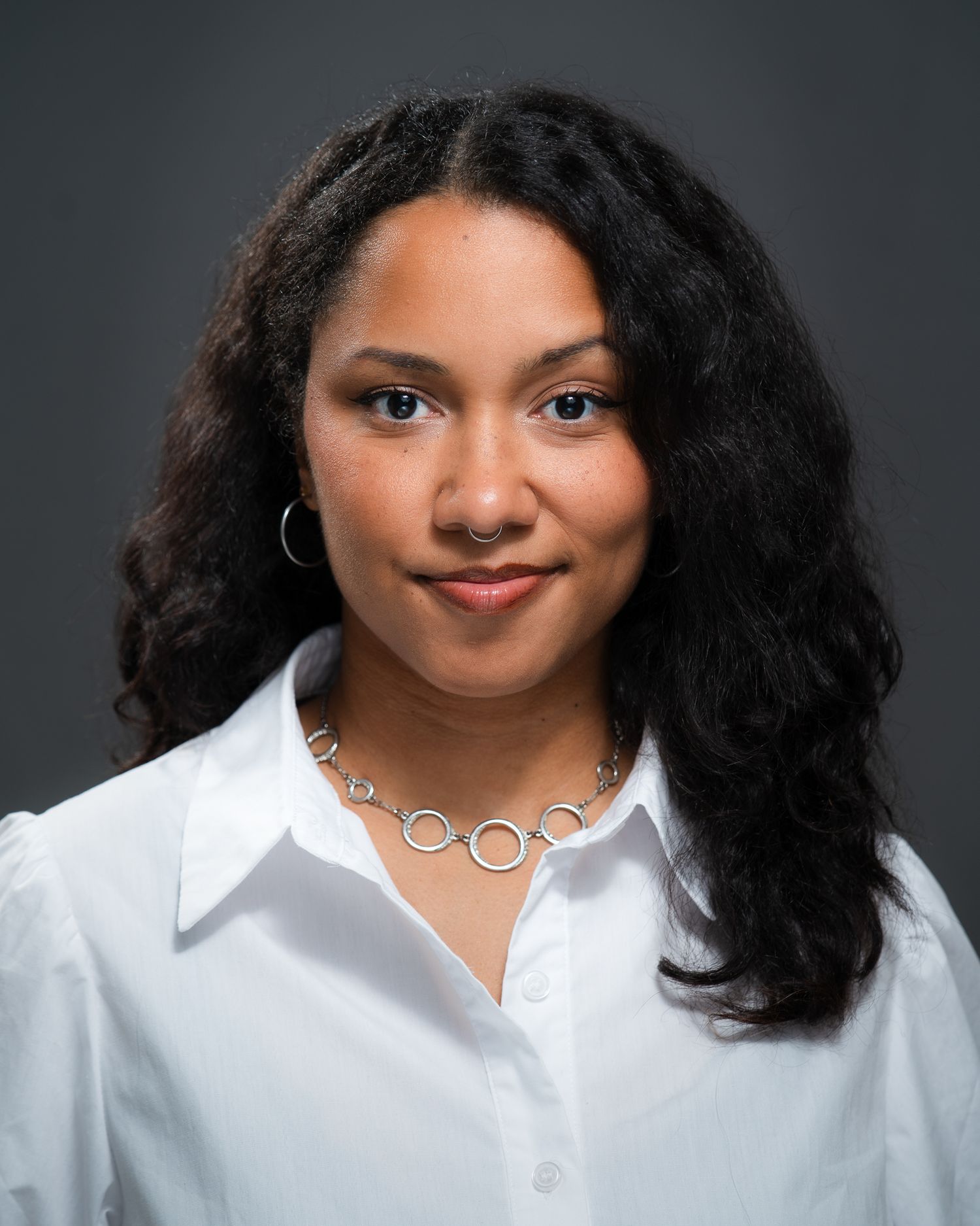 Studio portrait of a woman with curly hair wearing a white blouse, headshot photography by HAMIDI Photography.