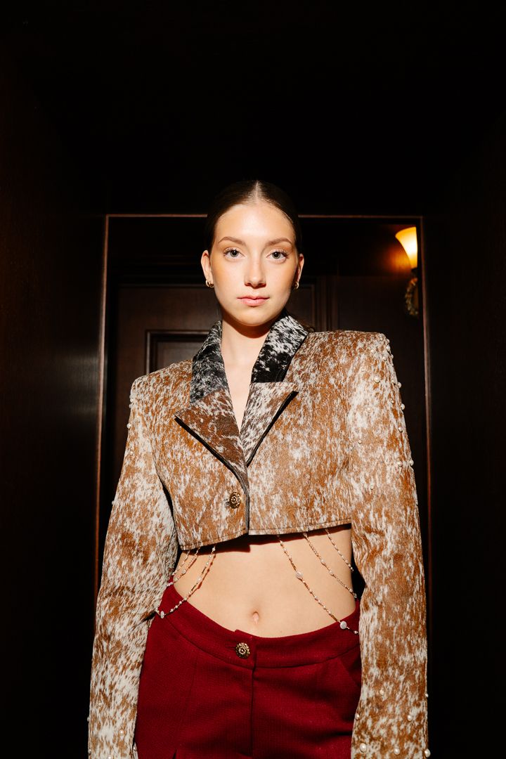 Model in an earth-tone coat and skirt under warm runway lighting, fashion photography by HAMIDI Photography.