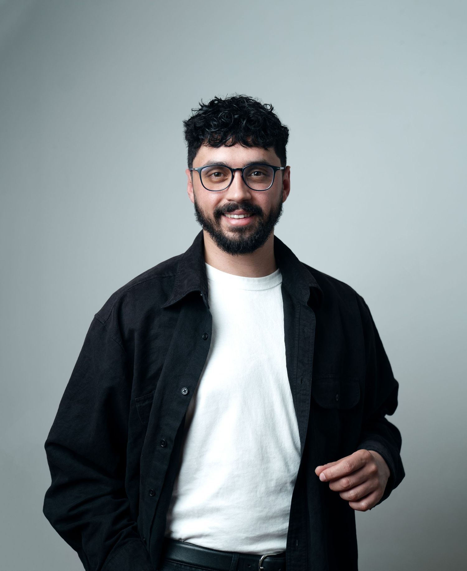 Studio portrait of a man in a black jacket and white t-shirt against a gray backdrop, headshot photography by HAMIDI Photography.