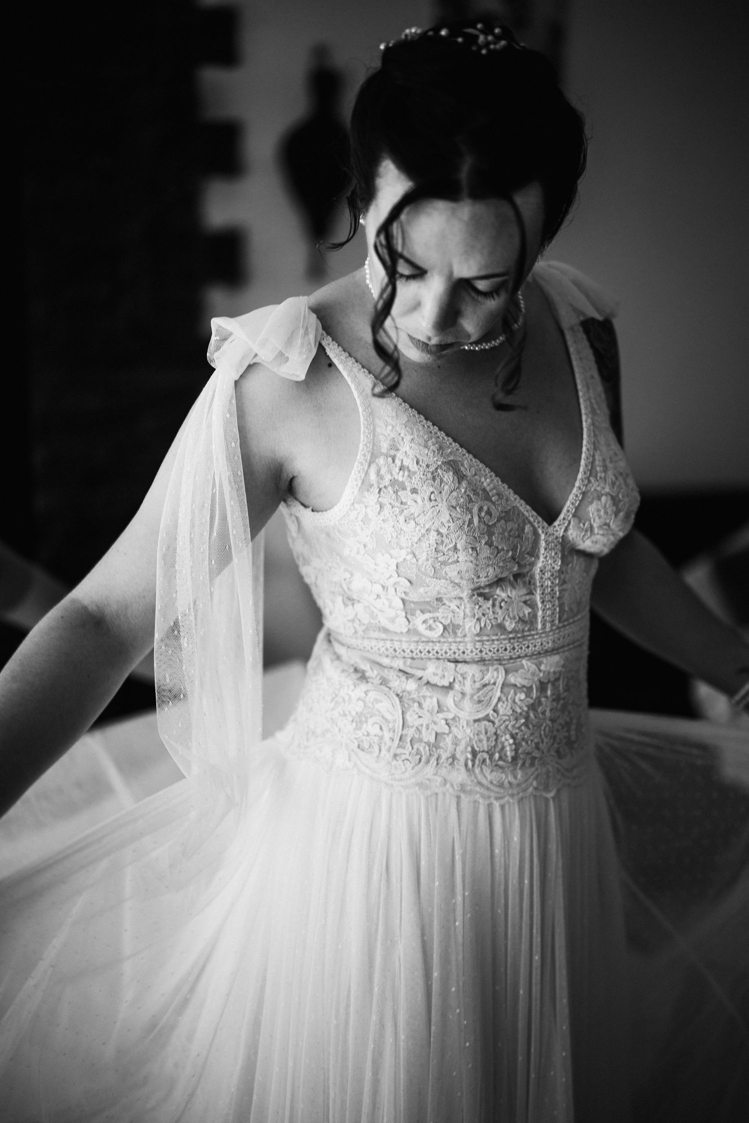 Black and white photo of a bride in a lace wedding gown with veil, looking down elegantly.