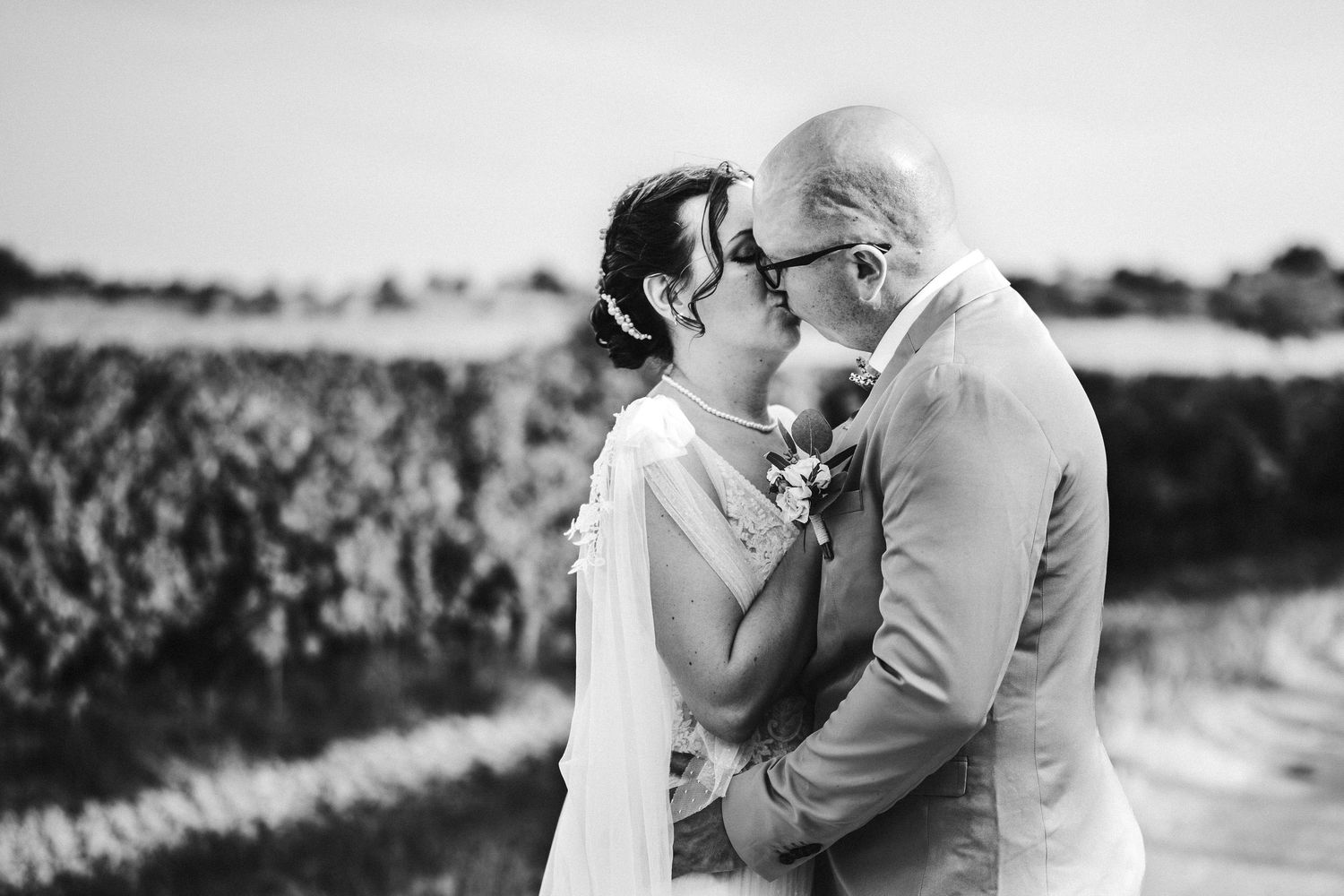 Black and white photo of a couple sharing a romantic kiss outdoors on their wedding day.