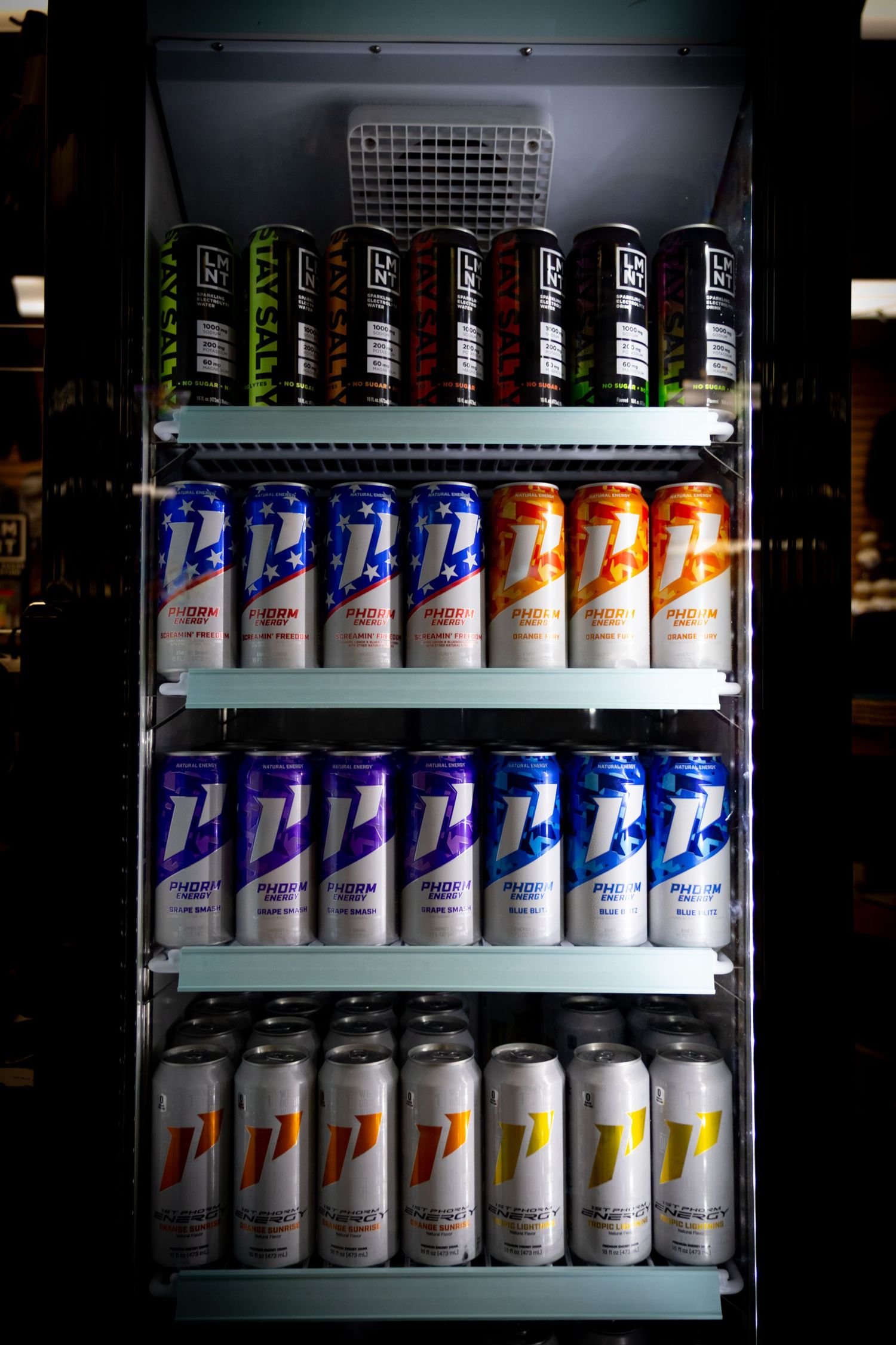Refrigerator display stocked with colorful energy drink cans including LMNT and Phorm brands.