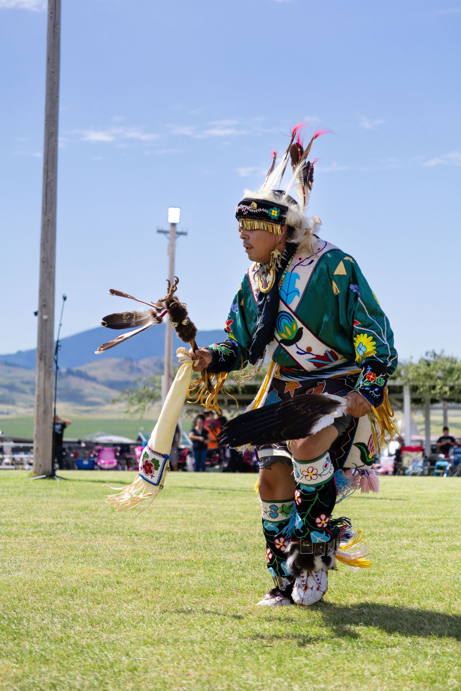 Native American dancer in traditional regalia performing at an outdoor powwow under blue sky.
