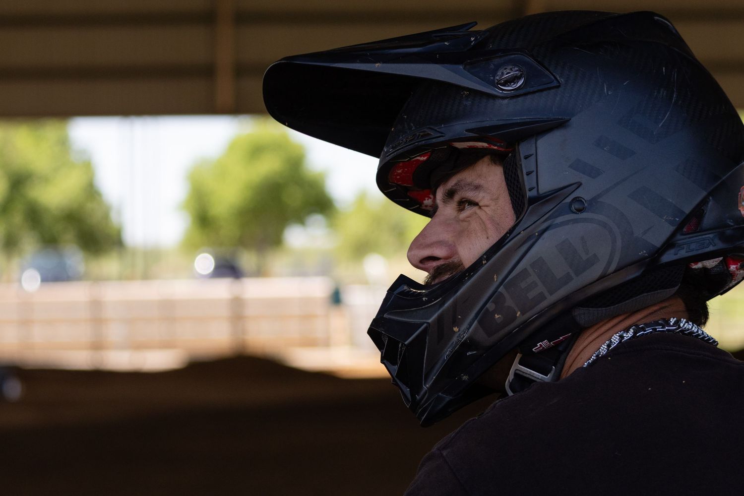 A motocross rider wearing a black full-face helmet looks over their shoulder in an outdoor arena setting.
