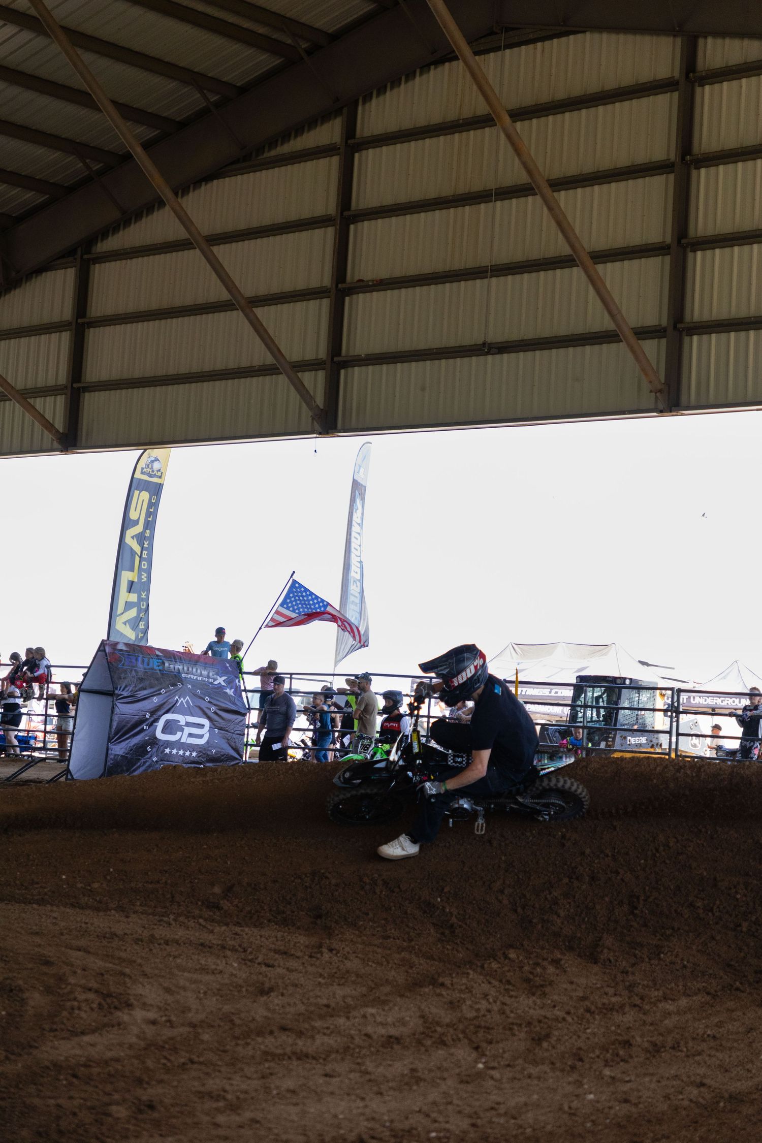 Motocross rider navigating a dirt track curve inside a covered arena with sponsor banners and spectators.