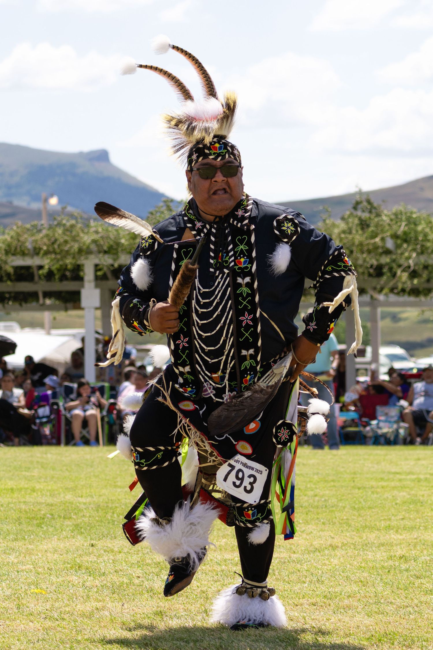 Native American dancer in traditional black regalia with feathers and beadwork performing at a powwow outdoors.