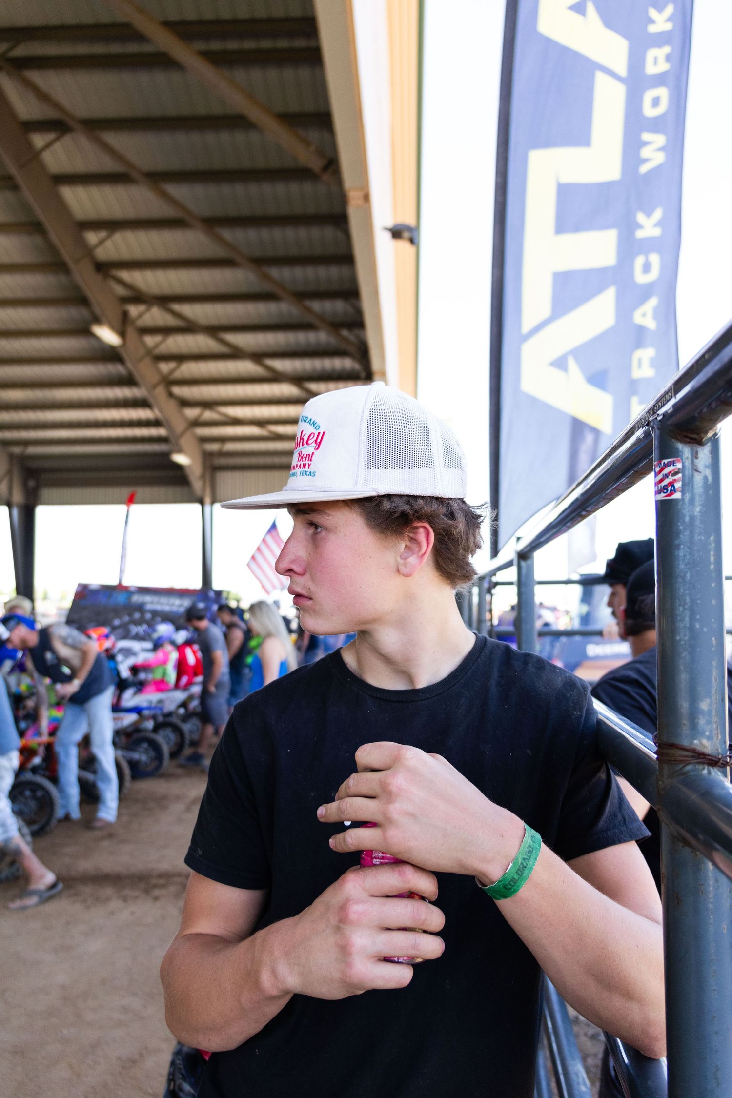 Young man in a white trucker hat watching motocross racing at an indoor dirt bike event near the track.