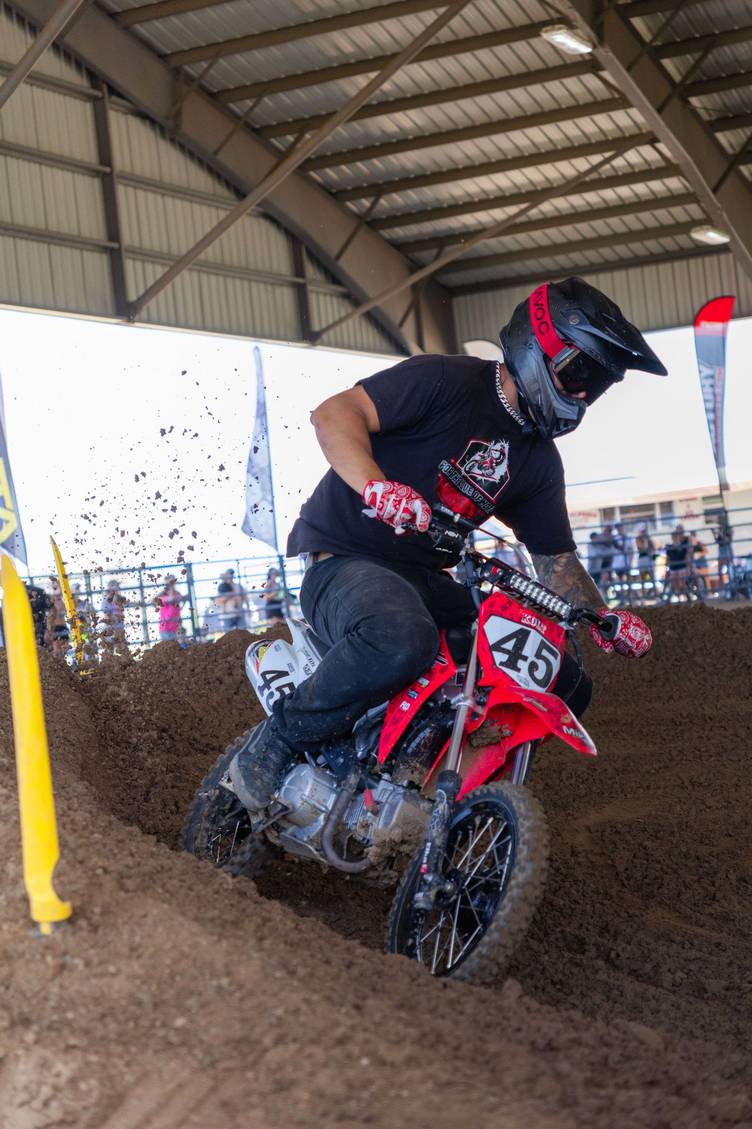 Rider number 45 powers through a dirt berm on a red Honda at an indoor motocross event.