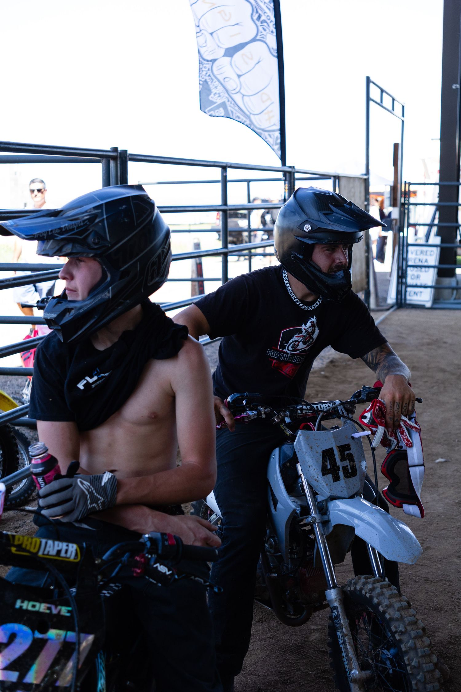 Two helmeted motocross riders stand with dirt bike #45 inside a covered arena staging area.