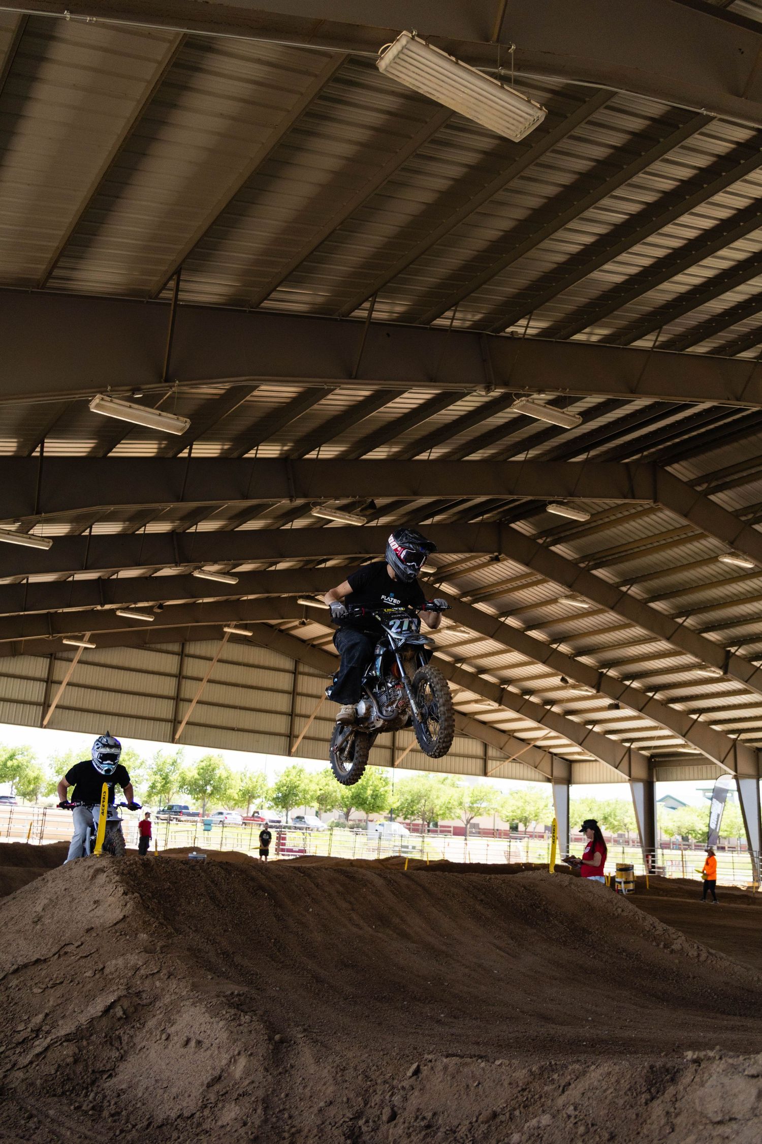 Motocross rider catches air on dirt bike jump inside covered arena at indoor motocross competition.