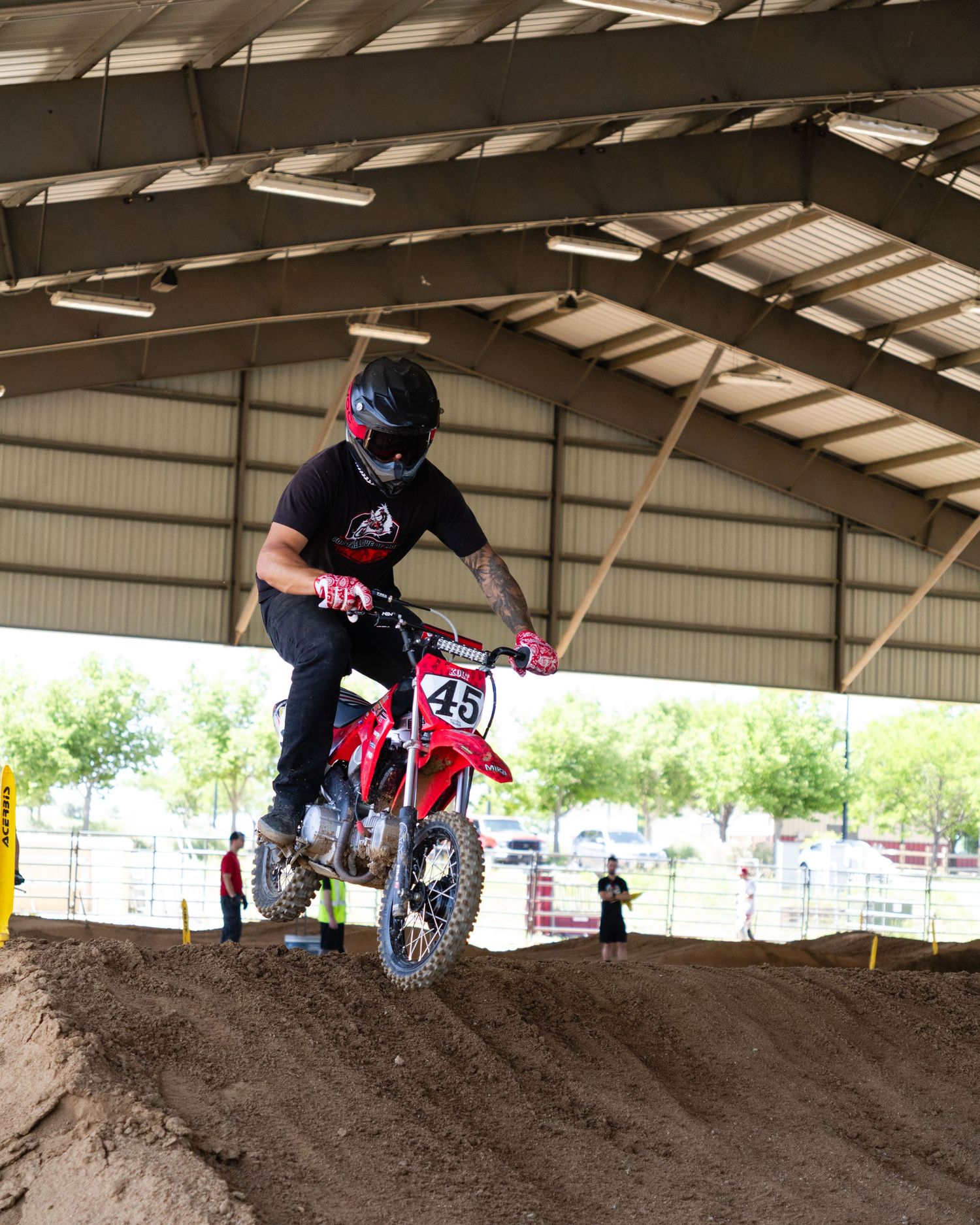 Motocross rider number 45 on a red Honda dirt bike jumping over a dirt mound in an indoor arena.