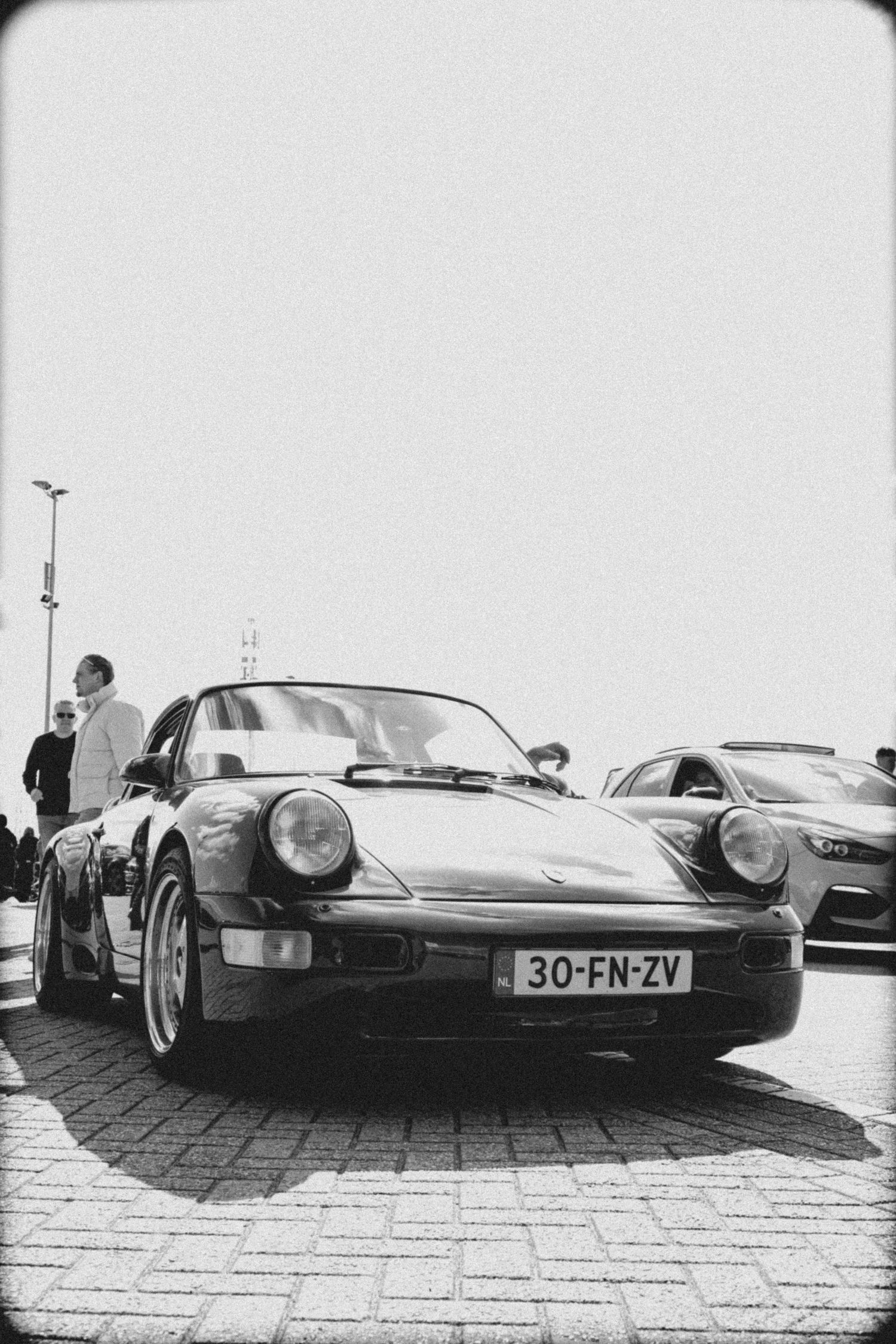 Vintage Porsche 911 with license plate 30-FN-ZV parked on cobblestones in black and white photography.