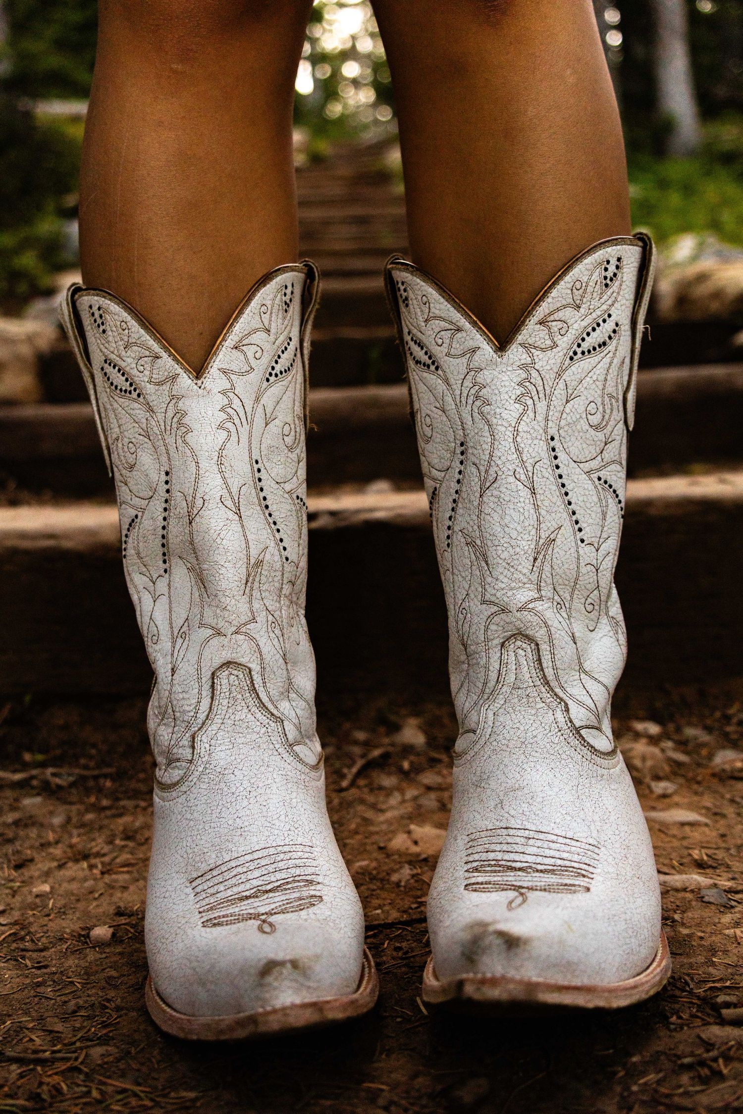 White embroidered cowboy boots with intricate stitching detail on a wooden surface.
