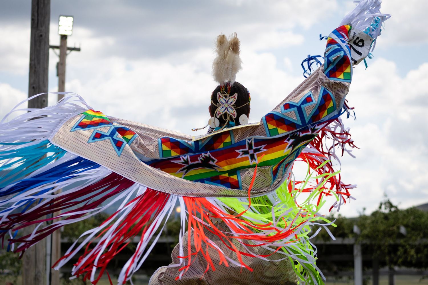 Colorful Native American regalia with rainbow fringe and geometric beadwork displayed at a powwow event.