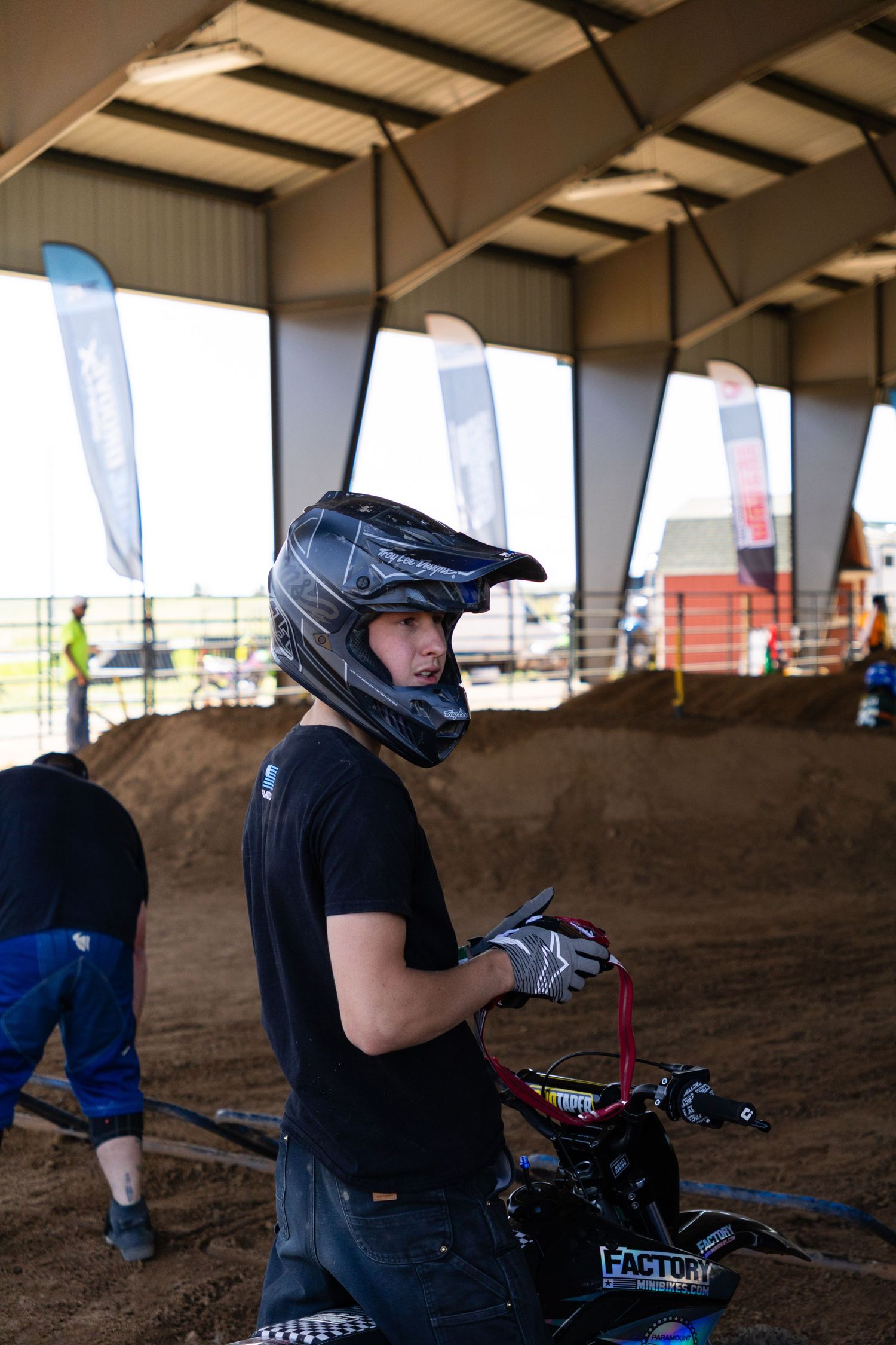 Young motocross rider in black helmet holding handlebars of a dirt bike at an indoor track.