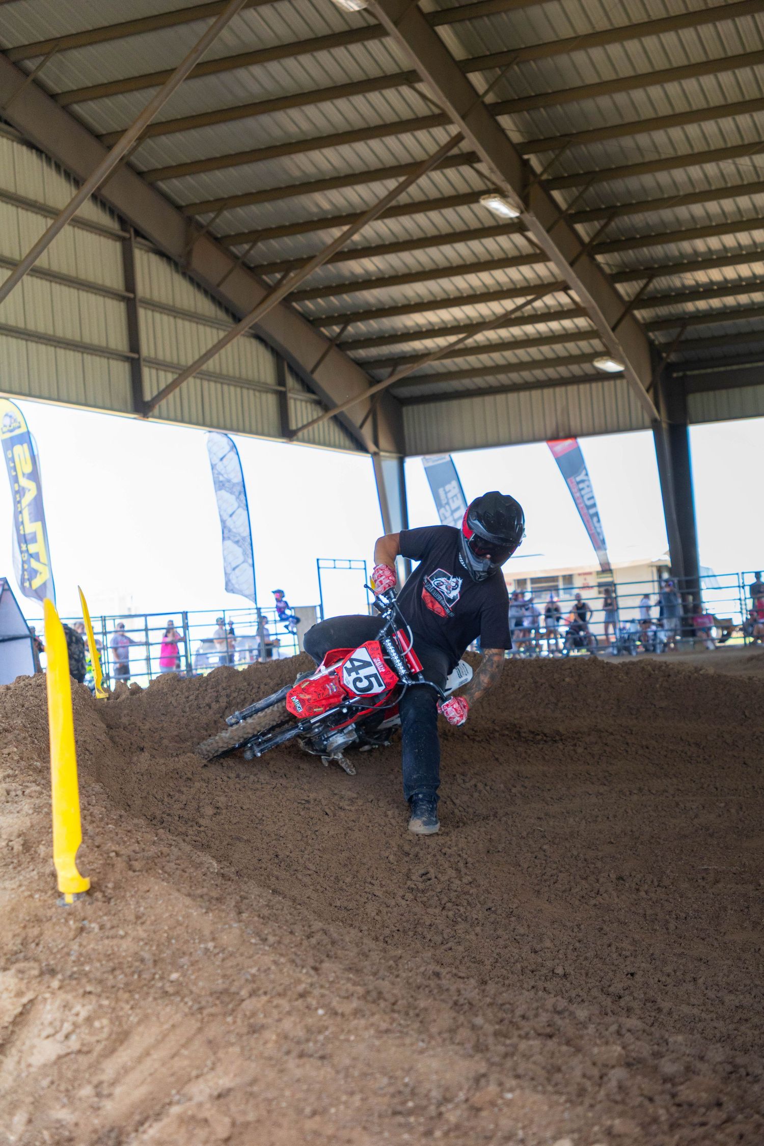 Motocross rider number 45 navigates a dirt berm on a red bike inside an indoor track.