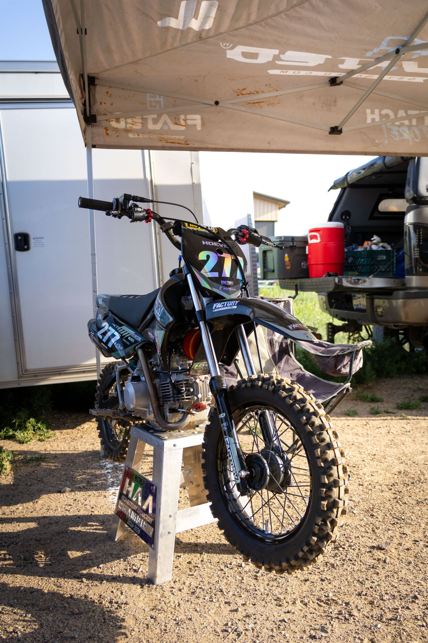 Black dirt bike number 27 displayed on a stand under a canopy at an outdoor motocross event.
