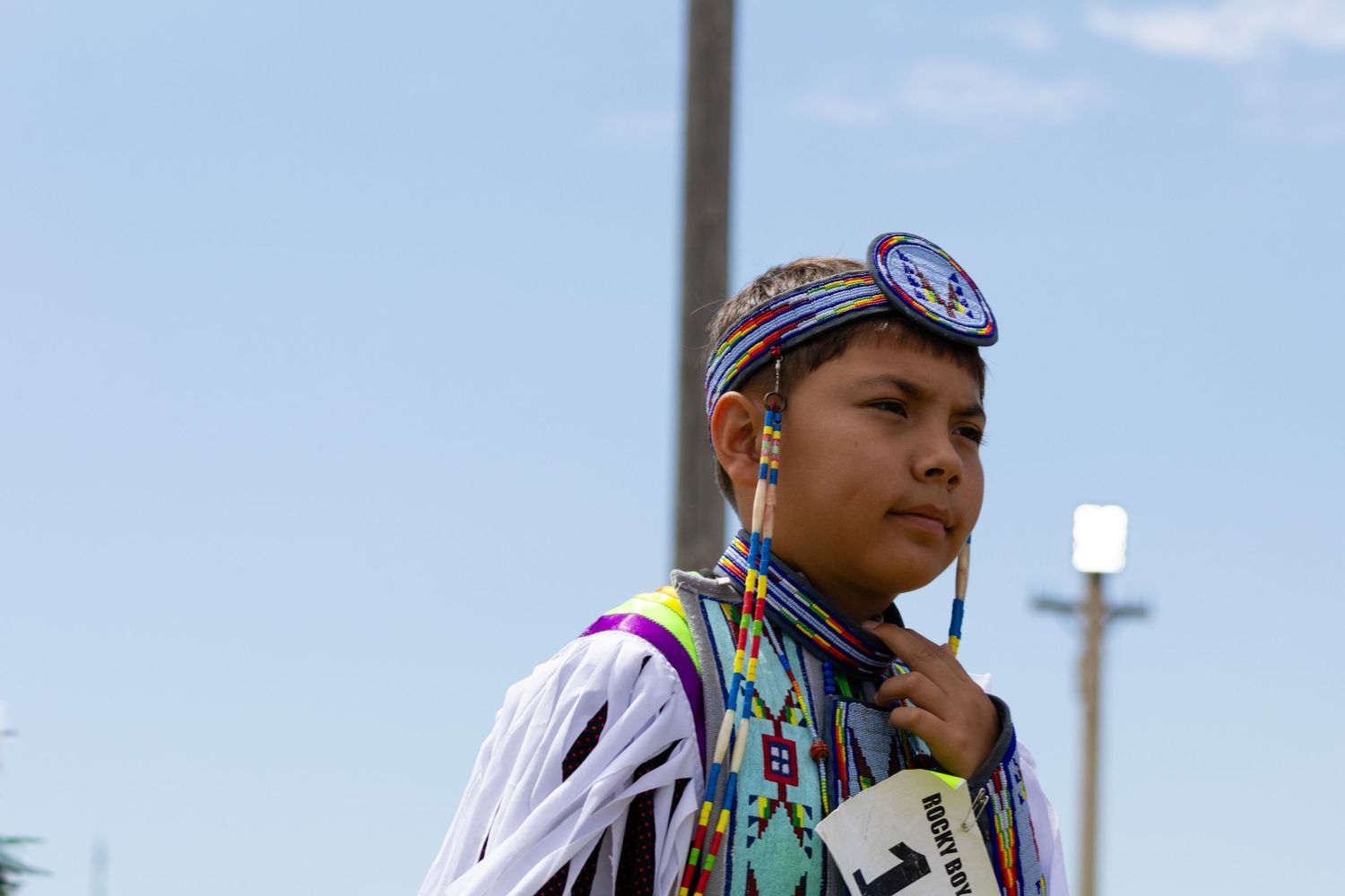 Native American youth in beaded regalia and headdress participating in a powwow dance.