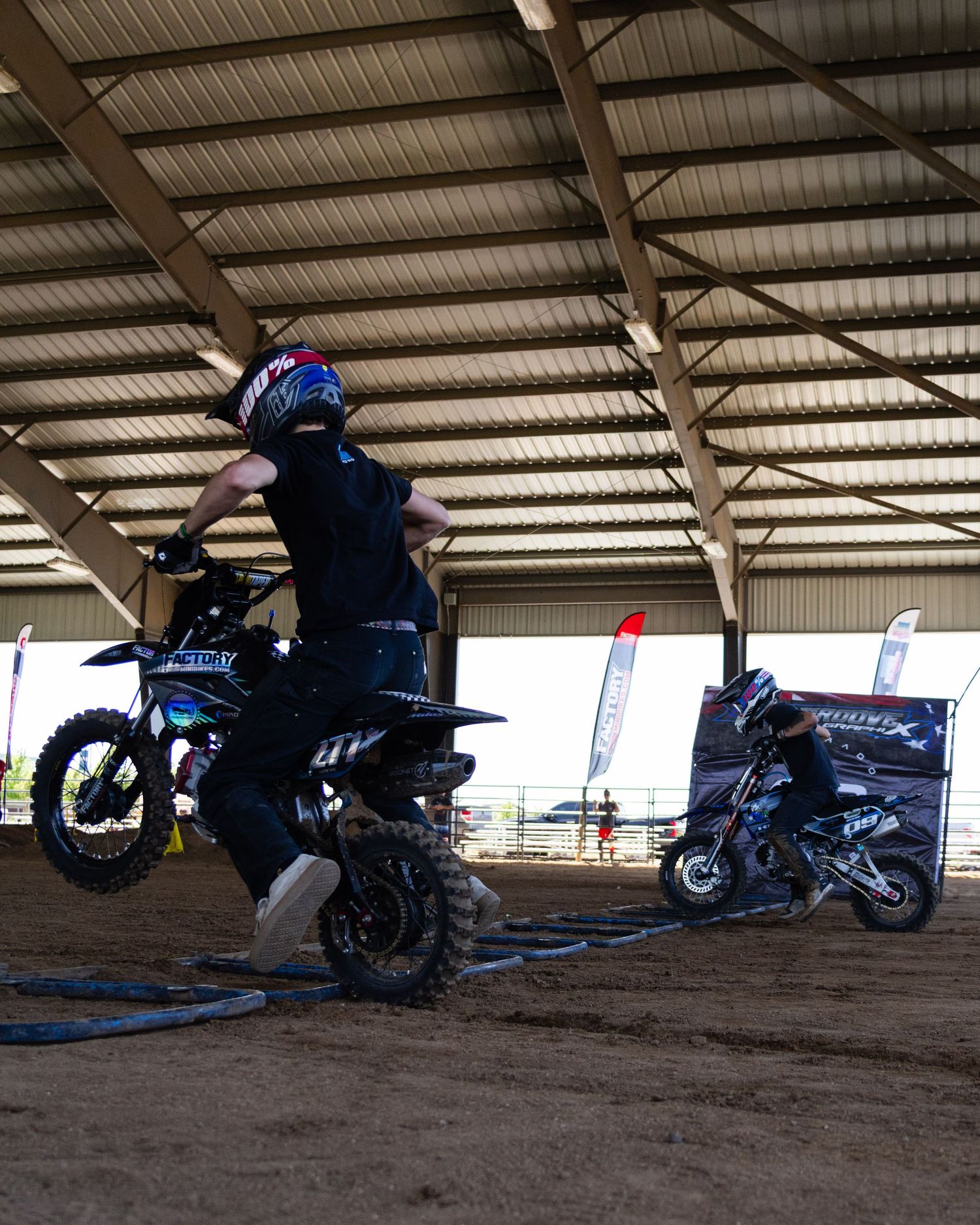 Motocross rider performs wheelie on dirt bike inside large covered arena at motocross event.